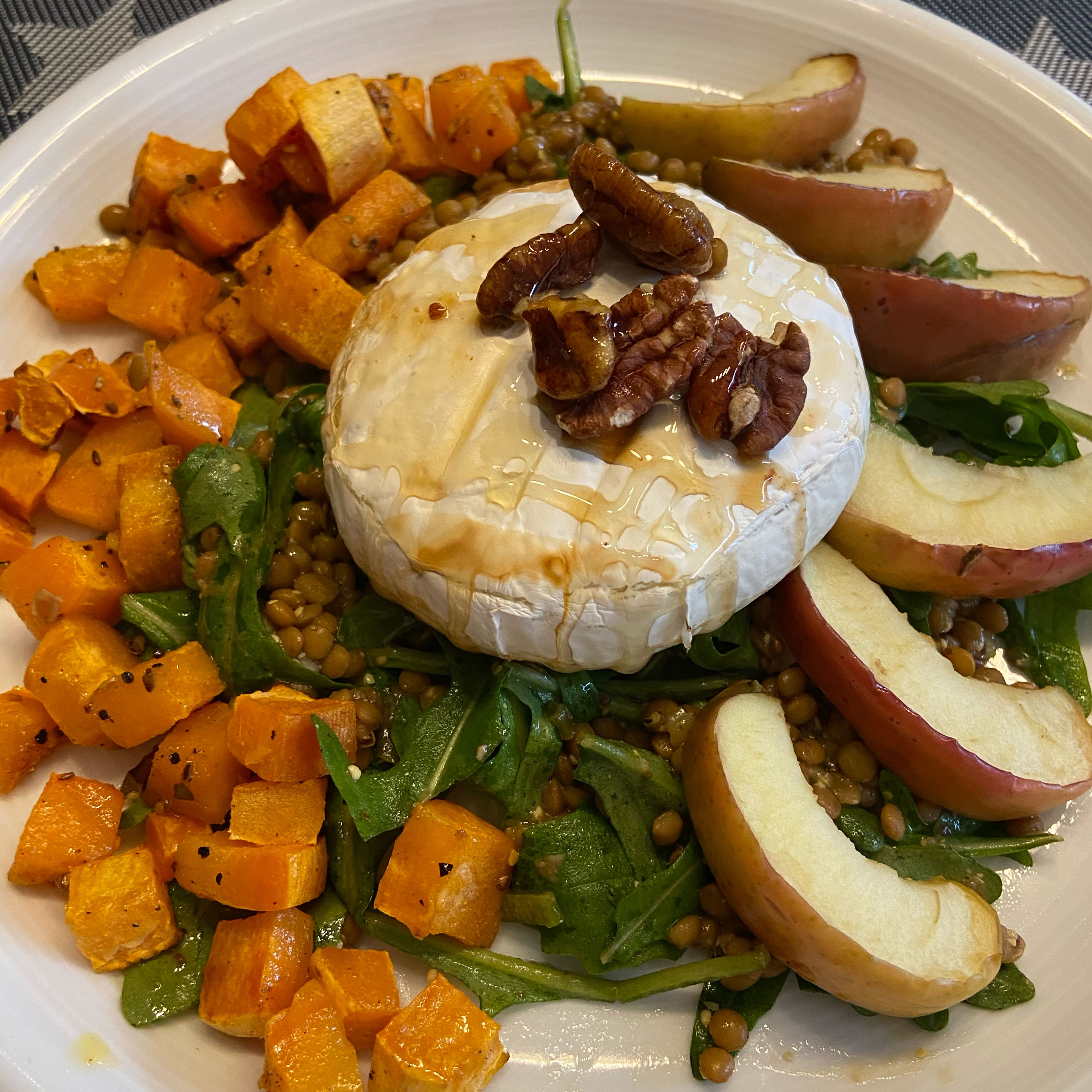 Nun den Linsensalat mittig auf einen Teller geben. Den Camembert in der Mitte auf dem Salat platzieren und mit den Pecannüssen dekorieren. Die Süßkartoffelwürfel und die Apfelspalten auf den Teller geben.