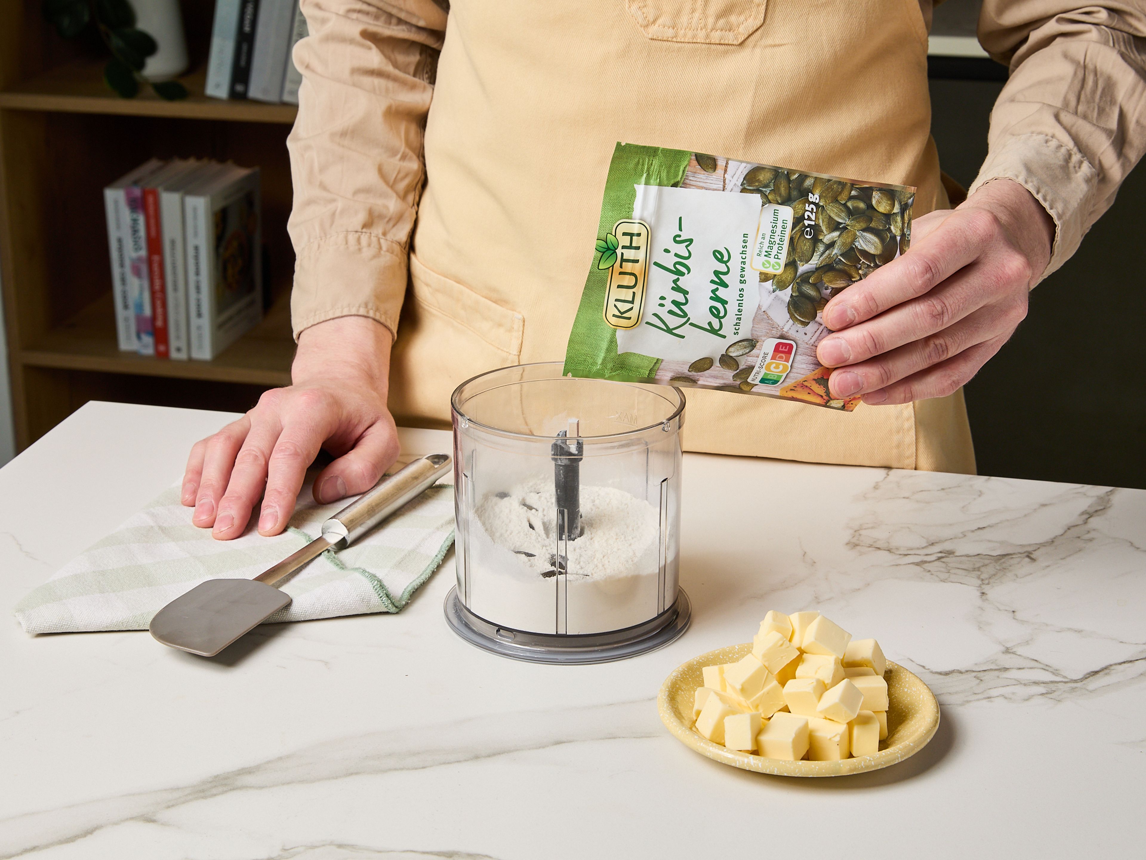 Den Backofen auf 180°C vorheizen. Für den Teig Mehl und die Hälfte der KLUTH Kürbiskerne in einem leistungsstarken Mixer zerkleinern, bis die Kürbiskerne fein gemahlen sind und das Mehl grün ist. Den Mehl-Mix mit Kürbiskernöl, gewürfelter Butter, Wasser und Salz in einer Küchenmaschine oder mit den Händen zu einem glatten Teig verkneten. Den Teig in Folie wickeln und ruhen lassen. In der Zwischenzeit die restlichen Kürbiskerne fein hacken und beiseitestellen.