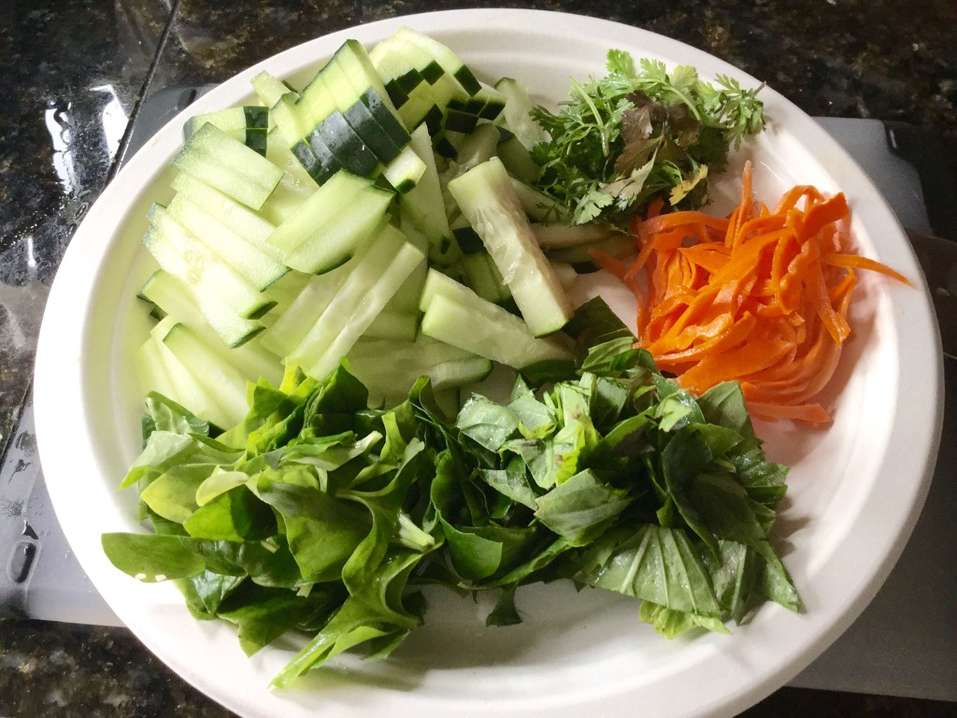 Eingelegte Karotten abgießen und Gurke, Thai-Basilikum, Kopfsalat und Koriander klein schneiden und beiseitelegen. Frühlingszwiebeln in Ringe schneiden. Pflanzenöl in einer Pfanne über mittlerer bis hoher Hitze erwärmen und Frühlingszwiebeln ca. 2 Min. anbraten.
