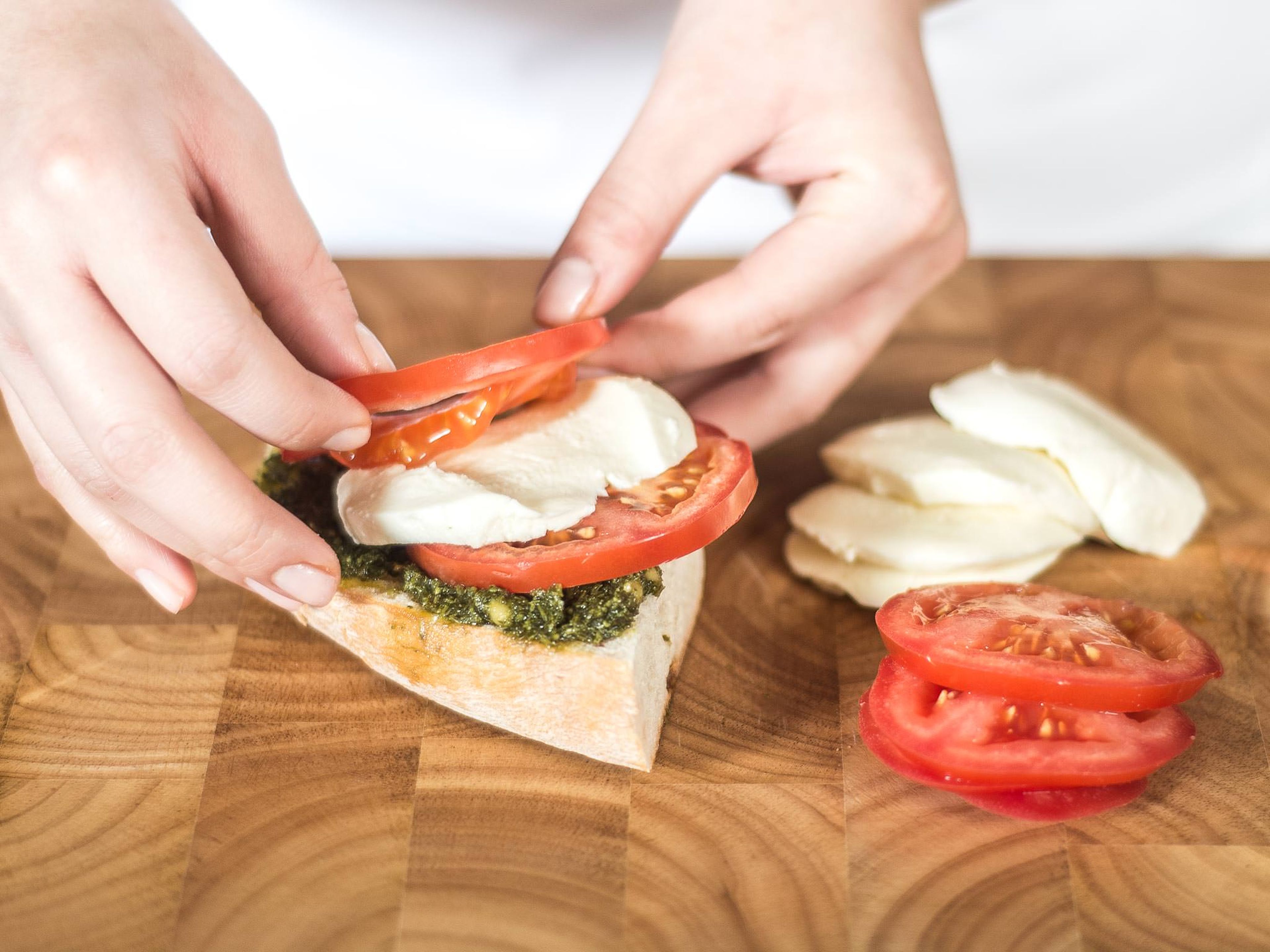 Next, spread the pesto onto the bread and place alternating layers of tomato and mozzarella slices on top.