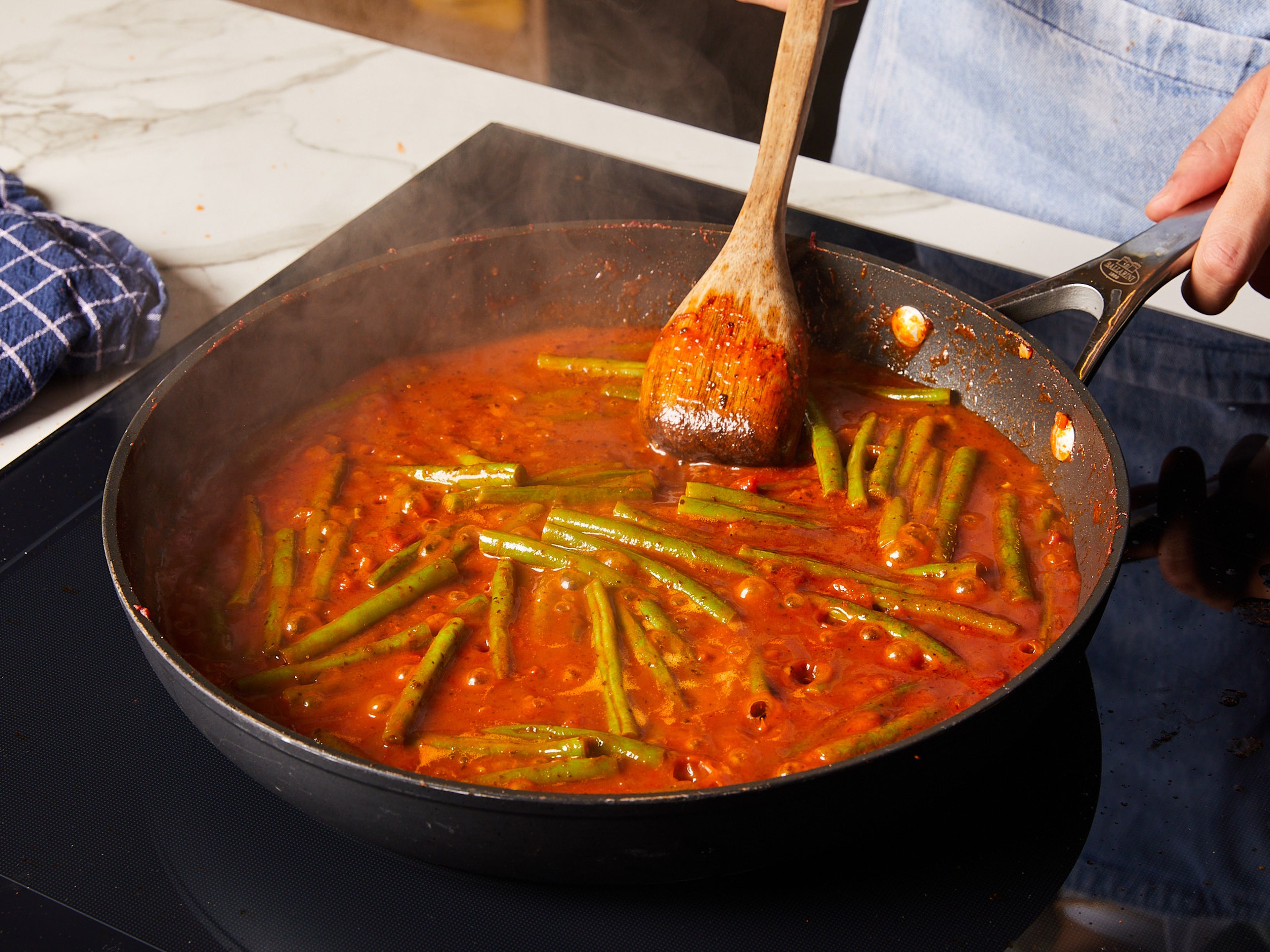 Währenddessen das Gemüse waschen. Die groben Spitzen der grünen Bohnen abschneiden und die Tomaten würfeln. Alles in die Pfanne geben und noch ein paar weitere Min. mitbraten. 
Wasser hinzugeben und umrühren. Den Deckel auf die Pfanne setzen und gelegentlich umrühren, bis die Bohnen durchgekocht sind. Wenn das Wasser zu schnell verdampft, bei Bedarf jedes Mal ca. 50 ml nachgießen. Nach Belieben mit Reis und Joghurt servieren.