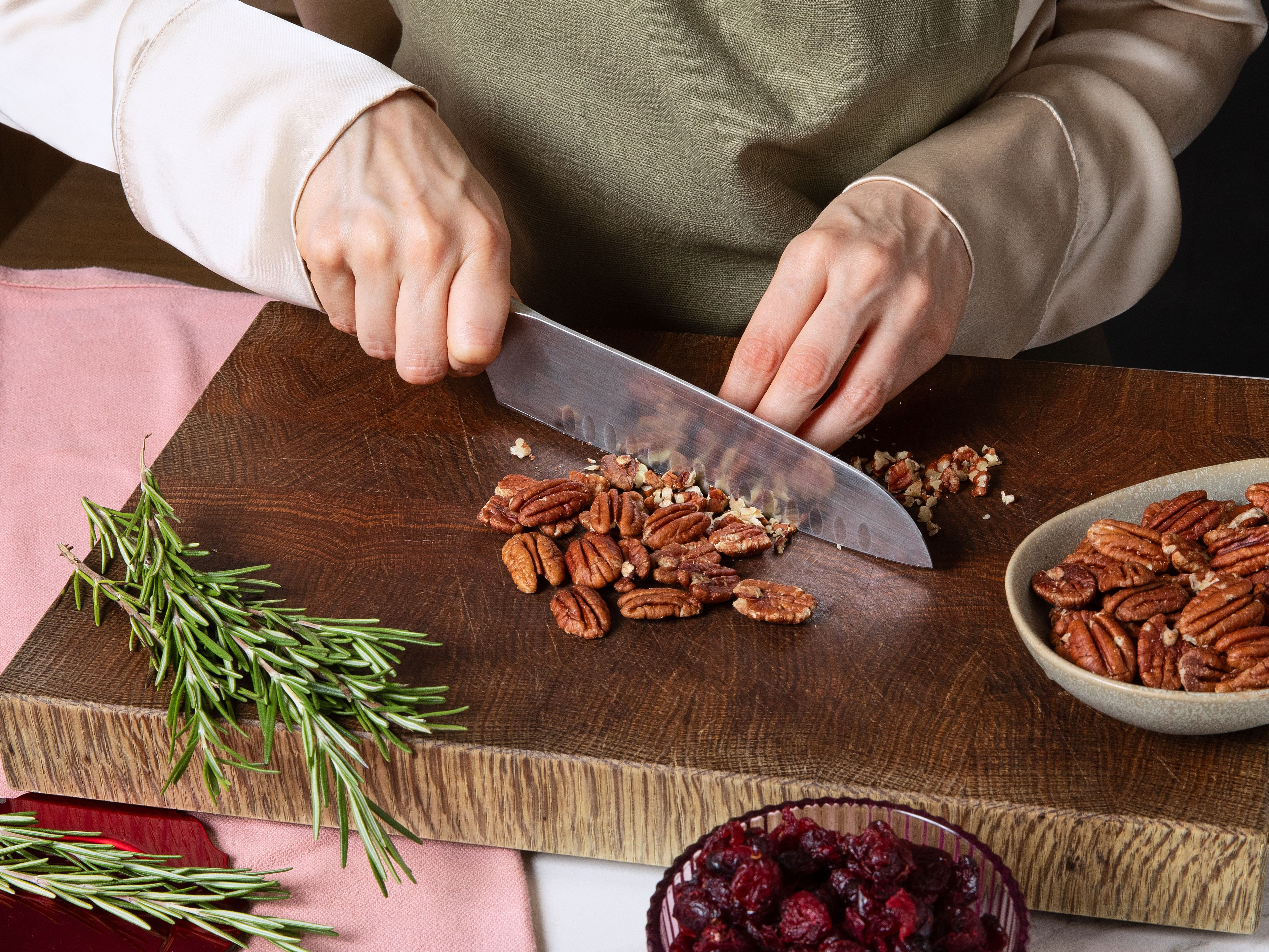 Ein Backblech oder einen großen Teller mit Backpapier auslegen. Die Pekannüsse grob hacken, die getrockneten Cranberrys fein schneiden und die Rosmarinblätter von den Stielen zupfen und fein hacken. Alles auf einem großen Teller oder in einer Schüssel mischen und mit etwas Salz und Pfeffer würzen.
