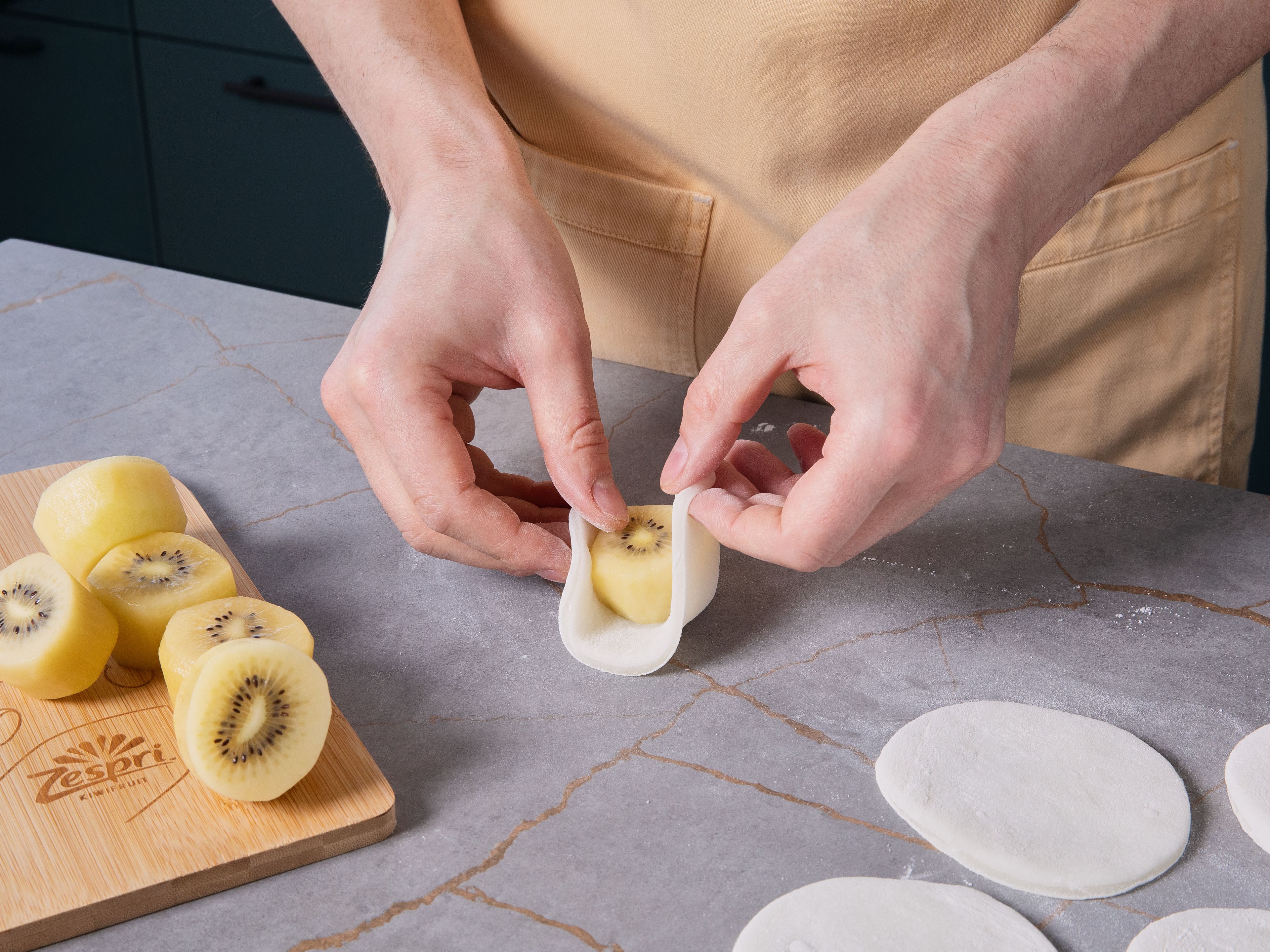 Zespri™ SunGold™ Kiwis schälen und an beiden Enden leicht anschneiden. Jeweils eine Kiwi mittig auf ein Teigstück setzen. Die Ränder nach oben ziehen und die Enden gut zusammendrücken, sodass kleine Mochi-Kugeln entstehen. Nach Bedarf mit den Händen rund formen und erneut mit etwas Stärke bestäuben, damit nichts klebt. Nochmals kühlen oder sofort servieren!