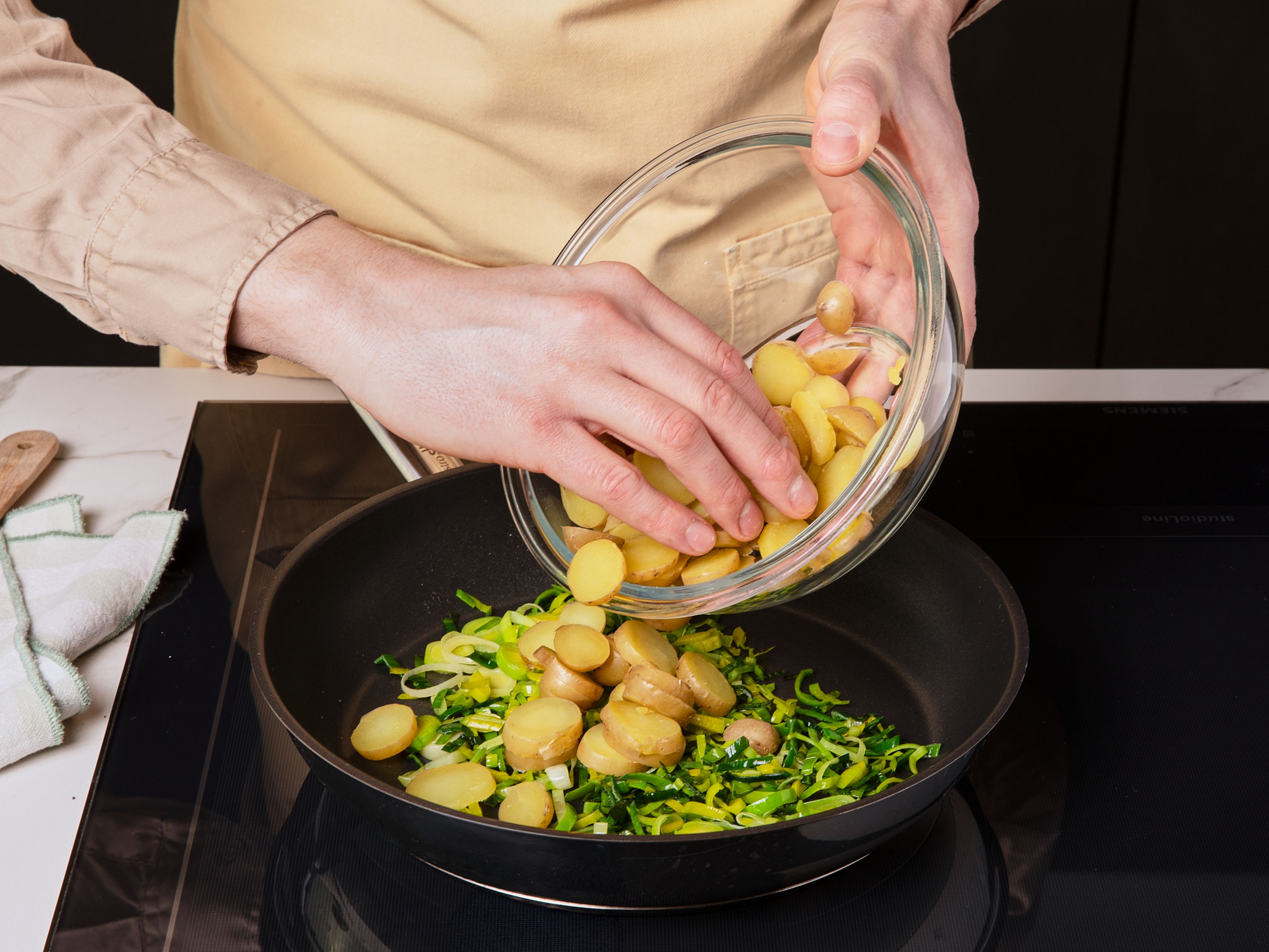 Für den Belag Kartoffeln in gesalzenem Wasser ca. 10–12 Min. bissfest kochen. Währenddessen den Lauch längs halbieren, waschen und quer in ca. 0,5 cm dicke Streifen schneiden. Die Lauchstreifen in einer Pfanne mit etwas Öl ca. 4–5 Min. anbraten, bis sie weich sind, aber noch keine Farbe haben. Nach Ende der Kochzeit die Kartoffeln unter kaltem Wasser abkühlen, in ca. 0,5 cm dicke Scheiben schneiden und mit dem angebratenen Lauch vermengen.