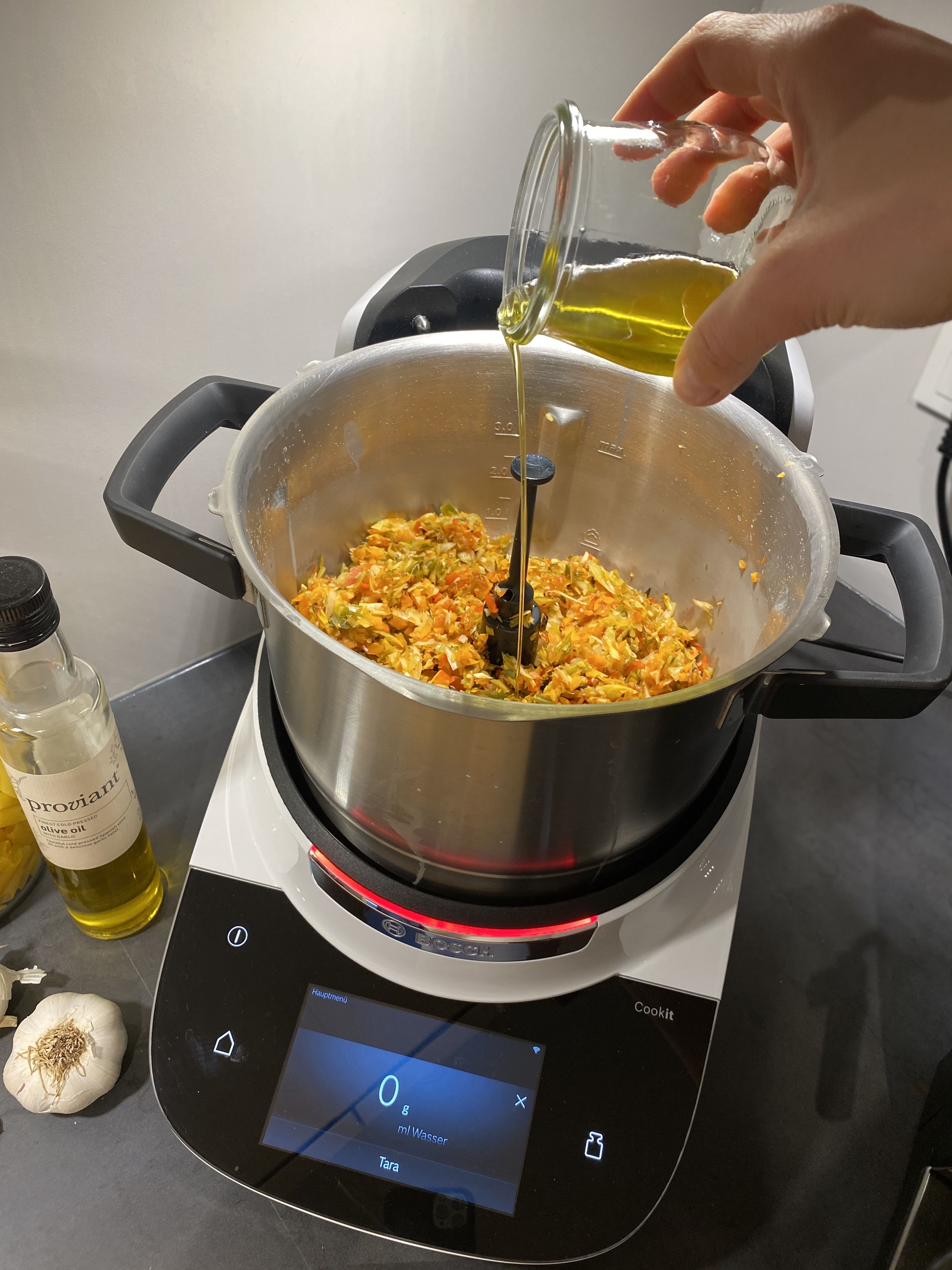 Das Universalmesser in den Cookit einsetzen und das gegarte Gemüse hineingeben. Anschließend die Waage aktivieren und ca. 60 ml Olivenöl hinzufügen.