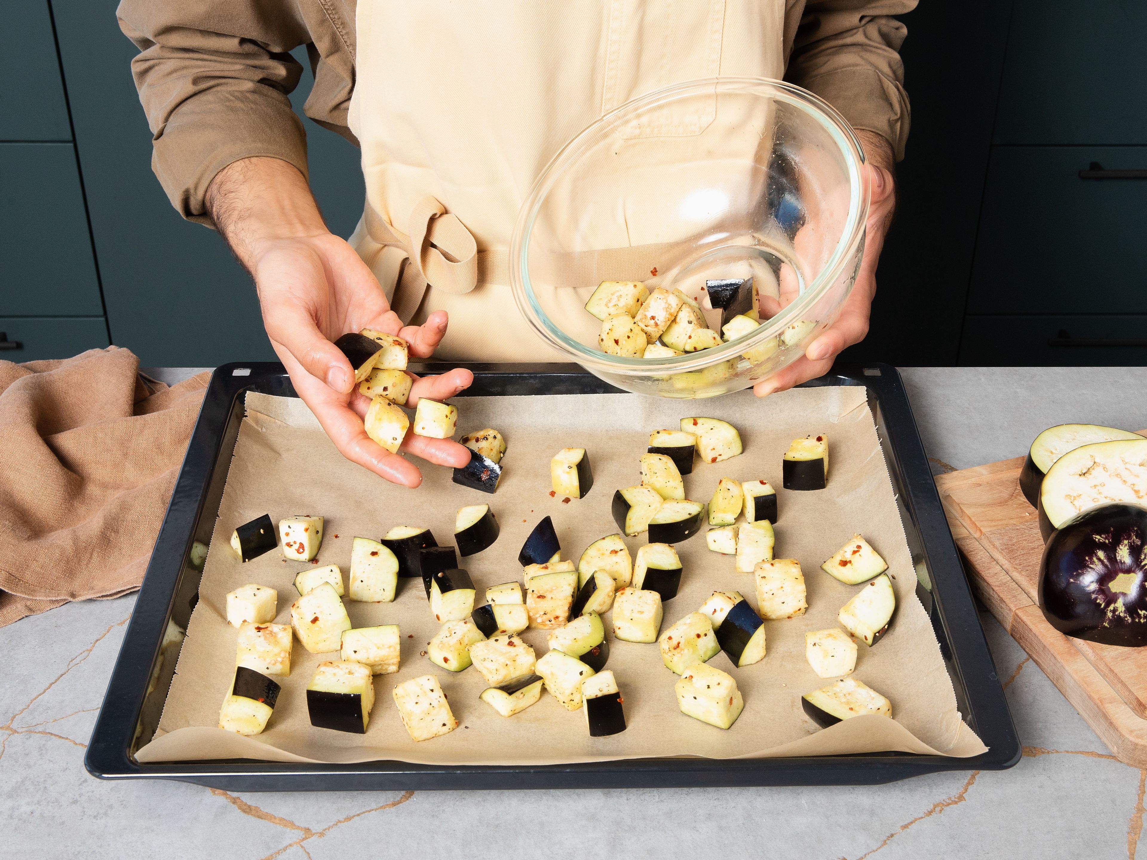 Preheat oven to 200°C/390°F. Cut stems off eggplants, and roughly dice them. Add diced eggplants into a bowl and toss with chili flakes, salt, pepper, and olive oil. Place pieces on a baking sheet lined with parchment paper. Bake for approx. 15 min. until soft on the inside with the edges slightly crispy.