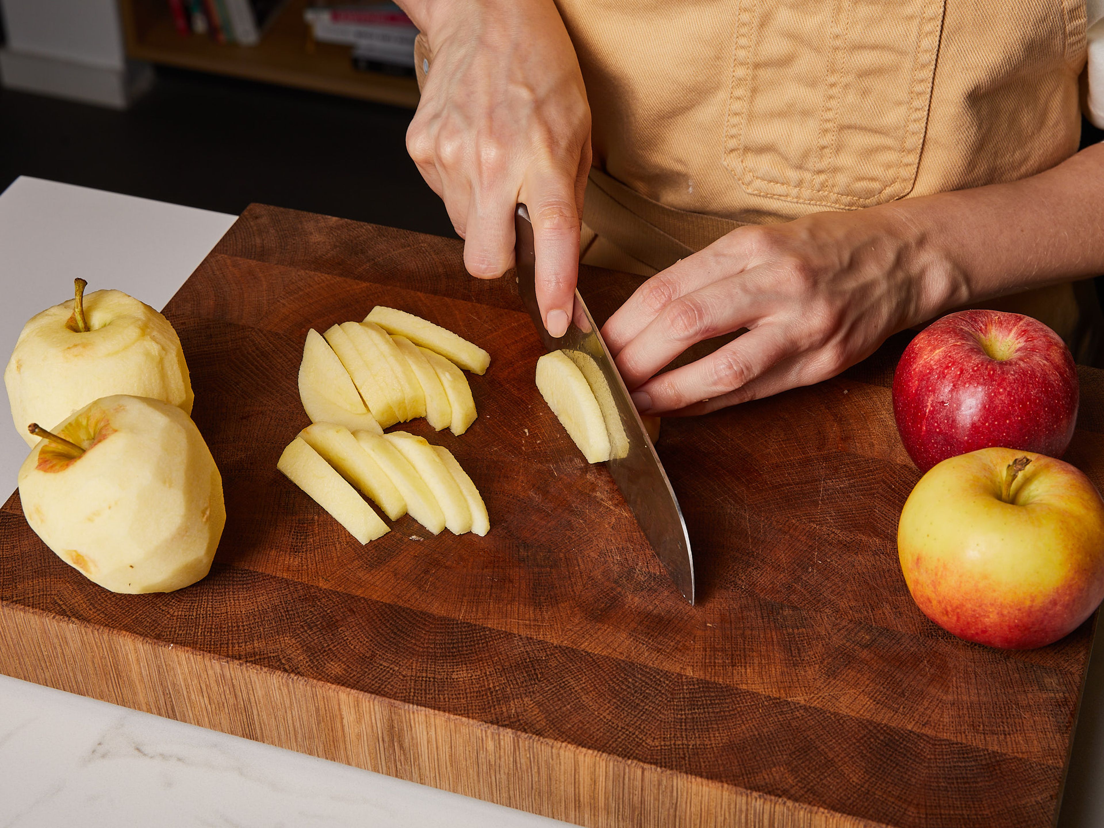 In der Zwischenzeit die Äpfel schälen, entkernen und in Scheiben schneiden. Die Apfelscheiben in eine große Schüssel geben, mit Zitronenschale und -saft vermischen und beiseitestellen.