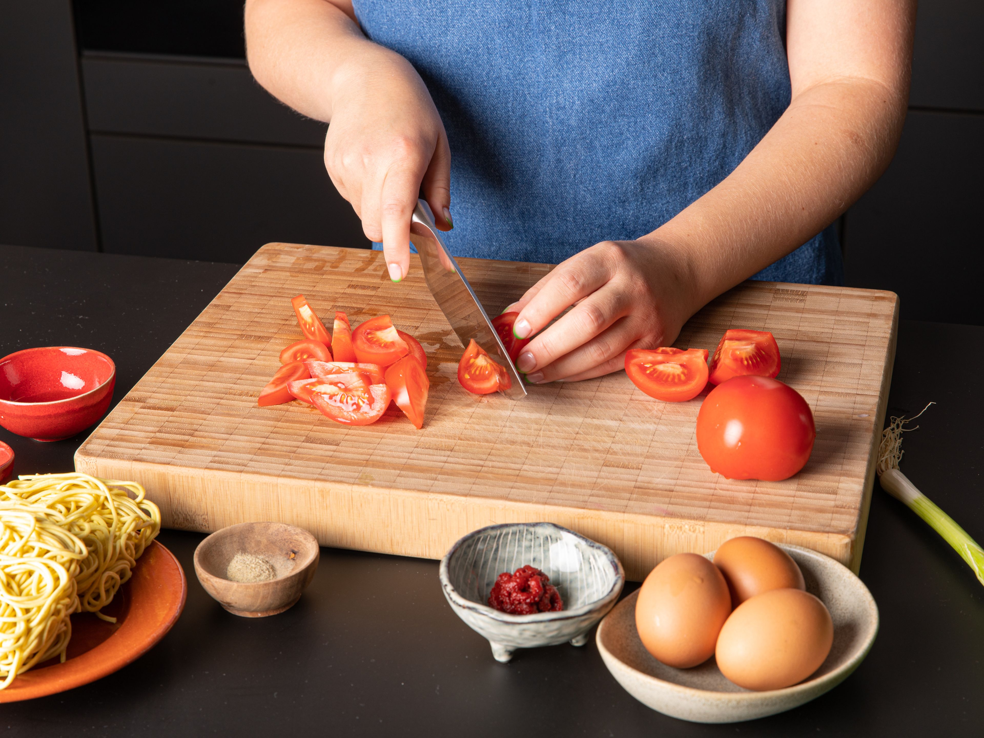 Tomaten in Spalten schneiden. Frühlingszwiebeln in Scheiben schneiden und die weißen und grünen Teile voneinander trennen. Knoblauch und Ingwer schälen und fein hacken.