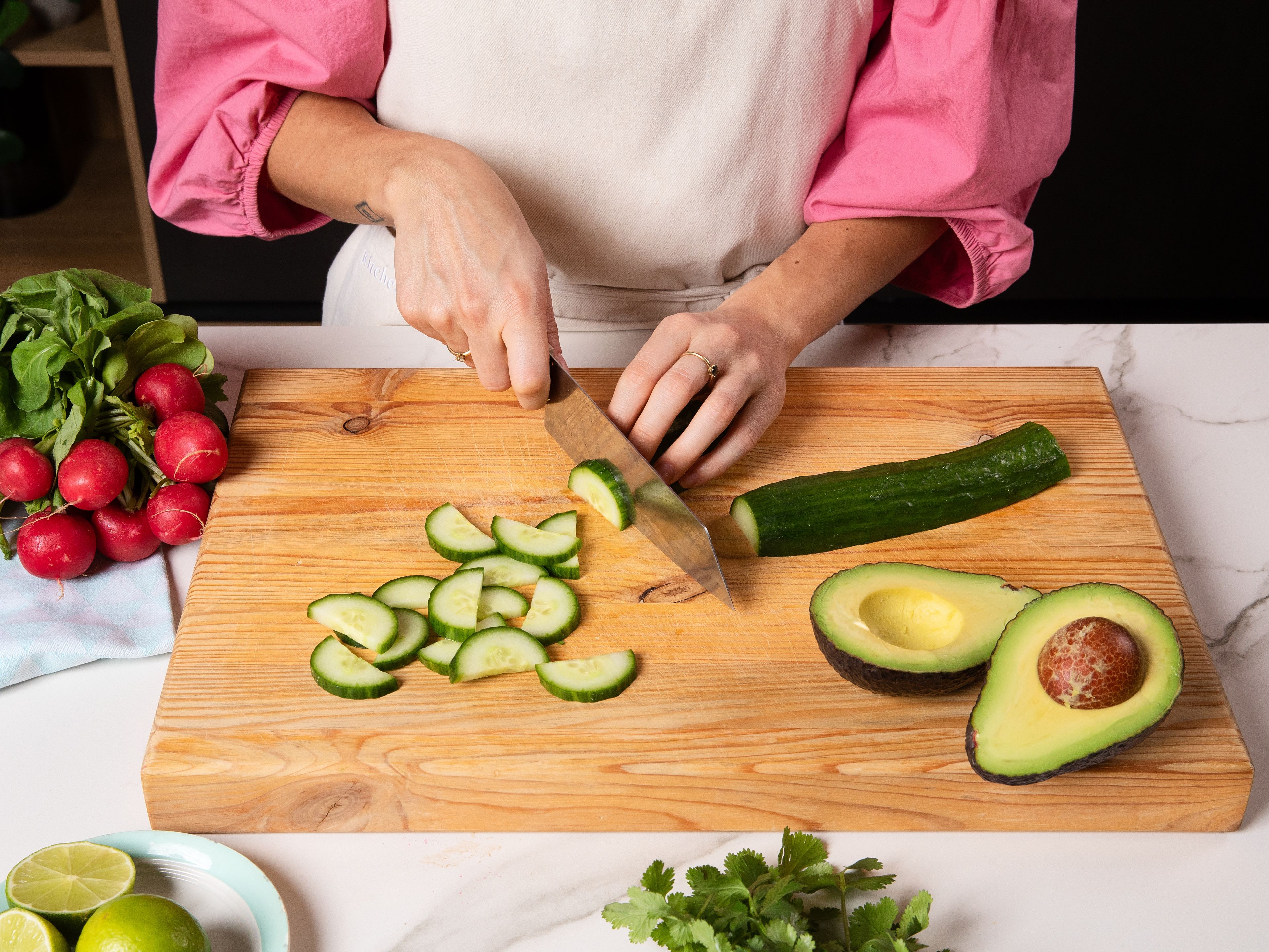 In der Zwischenzeit Edamame in kochendem Wasser ca. 3–5 Min. blanchieren, abgießen und ggf. aus den Schoten drücken. Gurke längs halbieren und in Scheiben schneiden, Radieschen in Scheiben schneiden. Avocado in Spalten schneiden. Frühlingszwiebeln in feine Ringe schneiden, Koriander grob hacken.