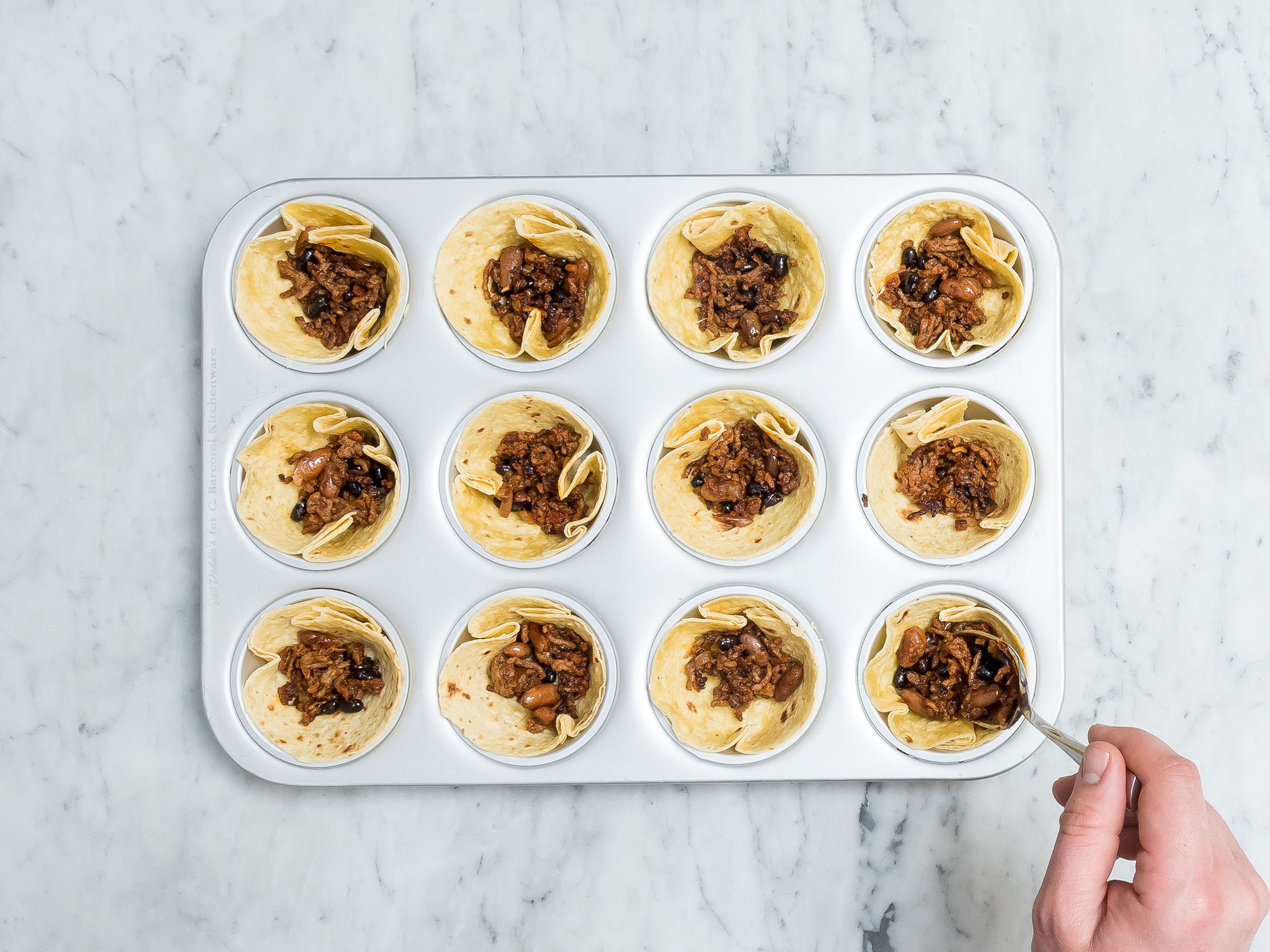 Cut corn tortillas into rounds to fit muffin tin cups, if necessary. Place rounds into muffin tin, so that tortillas form cups. Add beef-bean mixture to the taco cups and crumble feta cheese over it. Bake at 180°C/370°F for approx. 10 – 12 min.