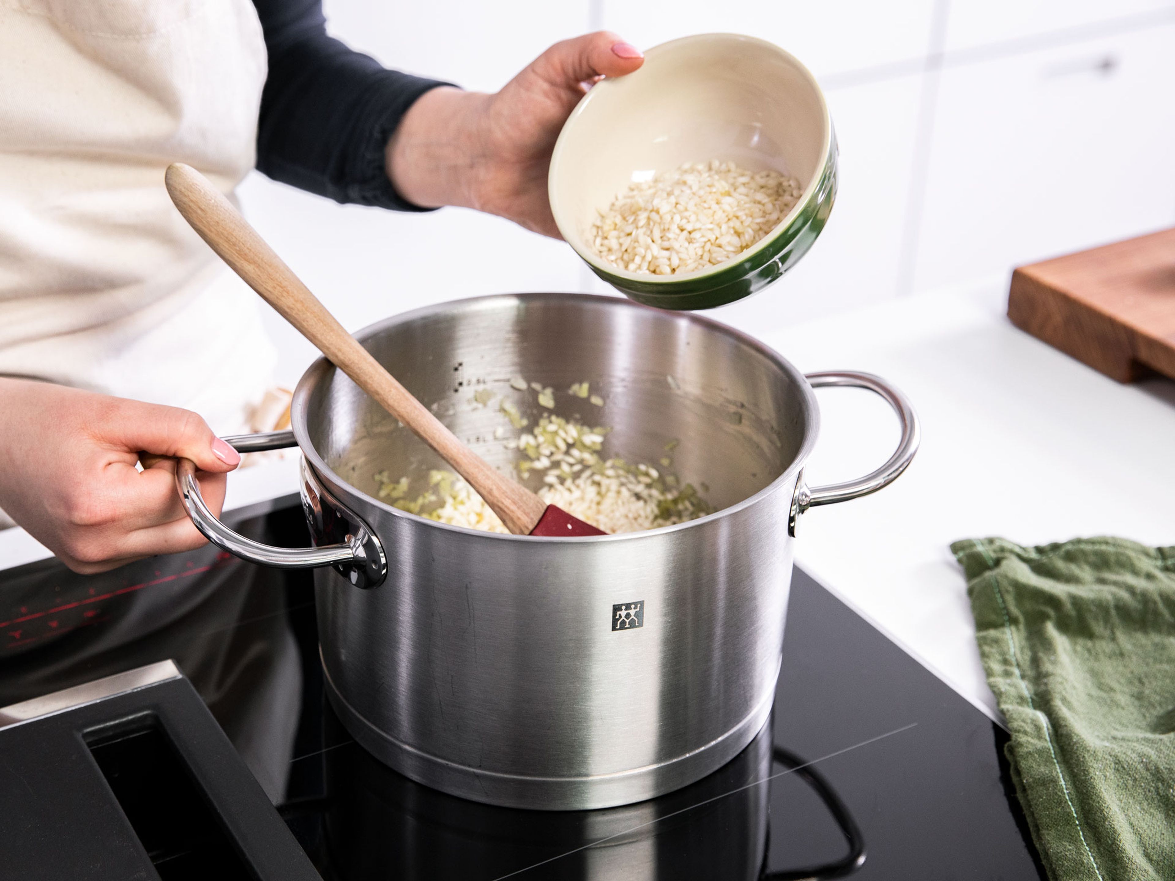 Zwiebeln und restlichen Knoblauch schälen und in feine Würfel schneiden. Restliches Olivenöl in einem großen Topf über mittlerer Hitze erwärmen und die Zwiebelwürfel darin ca. 1 Min. anschwitzen. Knoblauch dazugeben und ca. 2 Min. weiterbraten. Risottoreis dazugeben und ca. 1 Min. anschwitzen. Dabei gut umrühren, damit der Reis vom Olivenöl ummantelt wird.