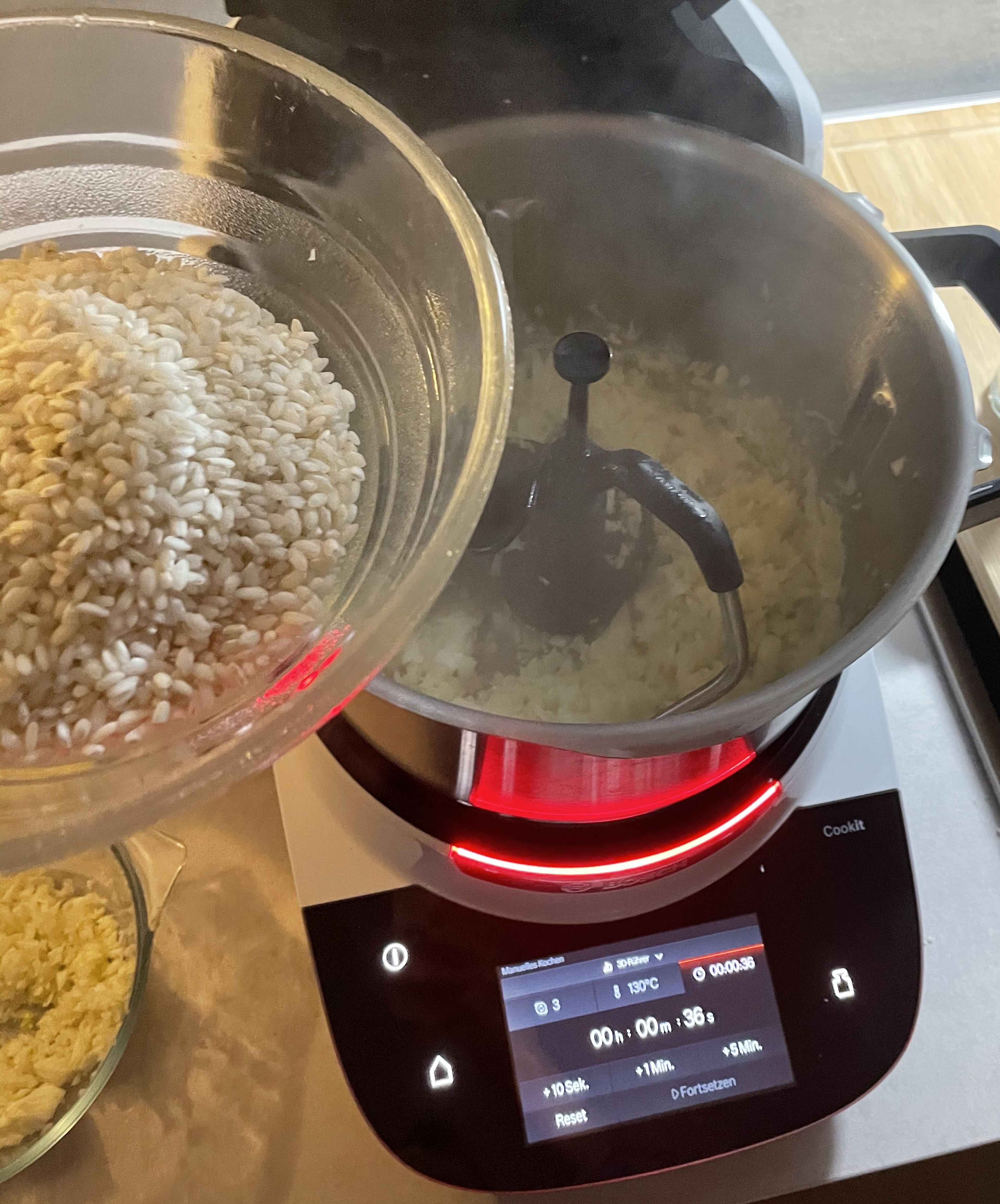 Die Zwiebel im Cookit bei geschlossenem Deckel und eingesetztem Messbecher fein hacken (Universalmesser | Stufe 14 | 15 Sek.) und mit dem Spatel vom Rand runterschieben. Das Universalmesser entfernen und den 3D-Rührer einsetzen. Dann 2 EL Öl und 2 EL Butter in den Cookit dazu geben und bei geschlossenem Deckel, ohne Messbecher, erhitzen (3D-Rührer | Stufe 3 | 120°C | 2 Min.). 2/3 des Fenchels in den Cookit geben und 1 Min. bei geschlossenem Deckel, ohne Messbecher, mitdünsten  (3D-Rührer | Stufe 3 | 120°C | 1 Min.). Danach den Risottoreis einwiegen, Deckel ohne Messbecher schließen und ca. 2 Min. braten, bis er schön mit dem Öl überzogen ist  (3D-Rührer | Stufe 3 | 120°C | 2 Min.).
