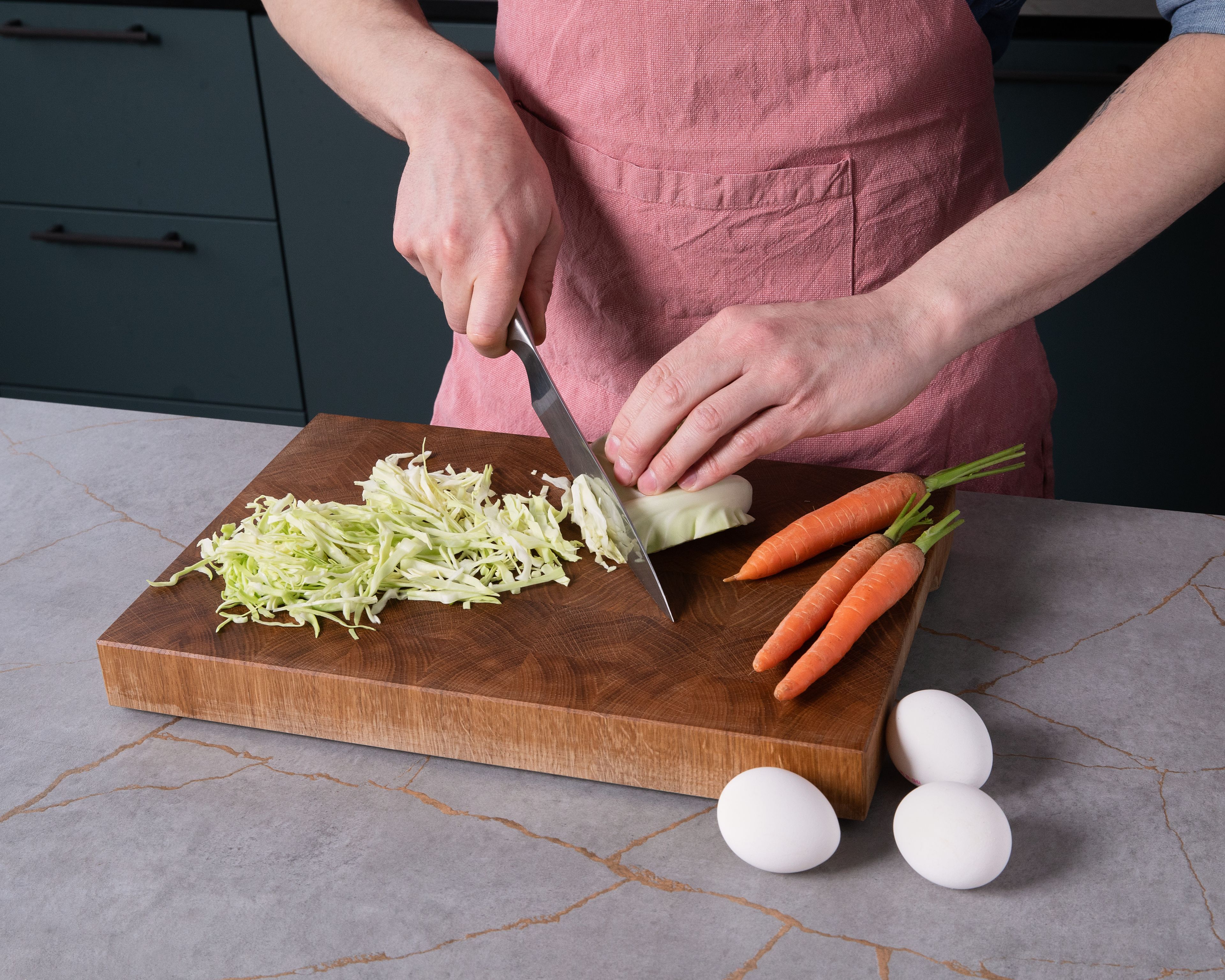 Den Backofen auf 230°C vorheizen und ein tiefes Backblech darin erwärmen. Währenddessen den Kohl in sehr dünne Streifen schneiden. Die Karotten schälen und grob reiben. Die Frühlingszwiebeln putzen und in dünne Ringe schneiden. Den Speck in kleine Stücke schneiden. In einer großen Schüssel die Miso-Paste im Wasser auflösen. Die Eier hinzufügen und verquirlen, dann nach und nach das Mehl unterrühren, bis ein glatter Teig entsteht.