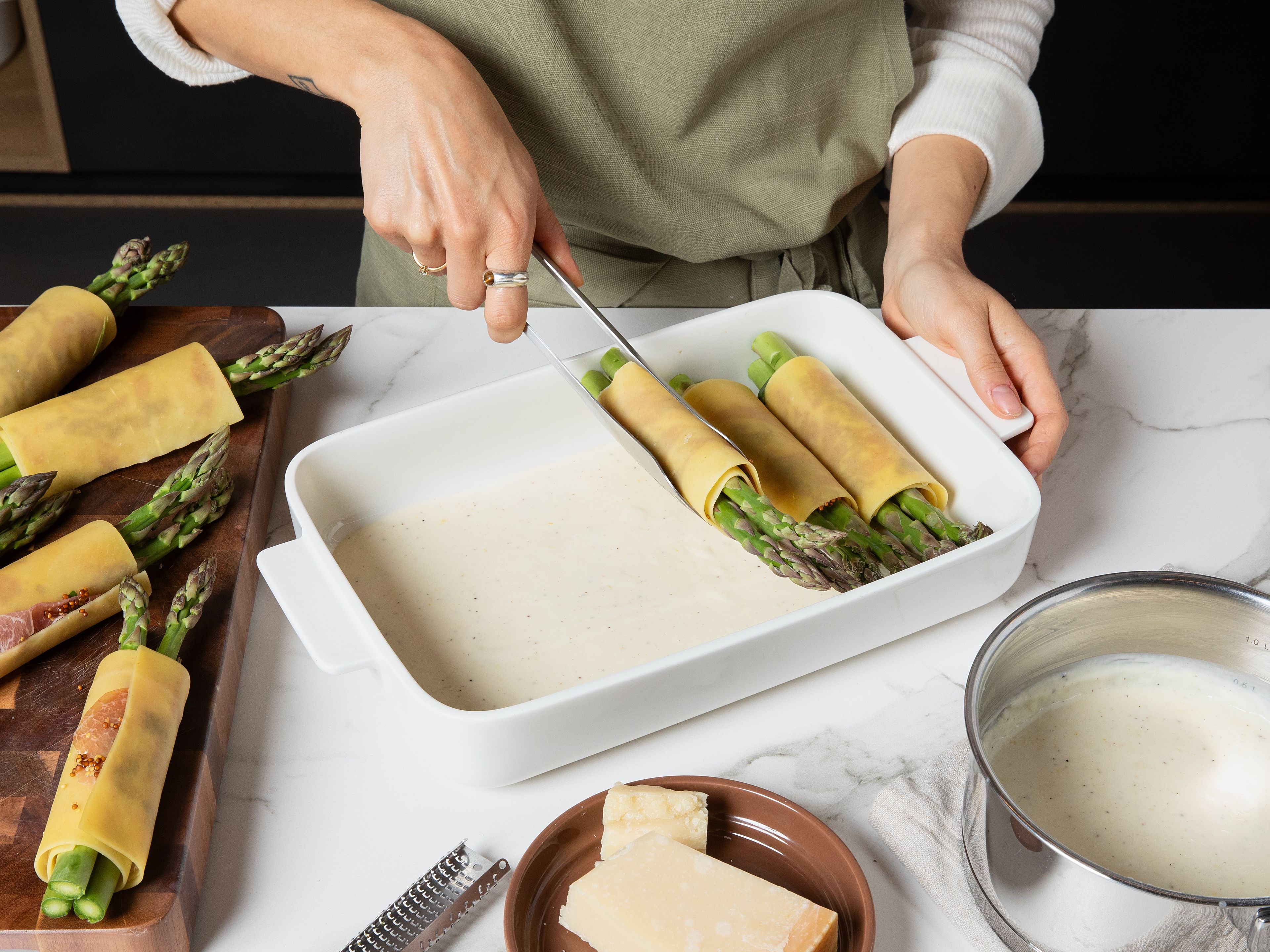 Spread half of the sauce in a baking dish. Arrange the cannelloni on top and cover with the remaining sauce. Sprinkle with freshly grated Parmesan and bake in the preheated oven for approx. 20–25 min., until golden and bubbling. Garnish with pine nuts, chives, and a little lemon zest before serving.