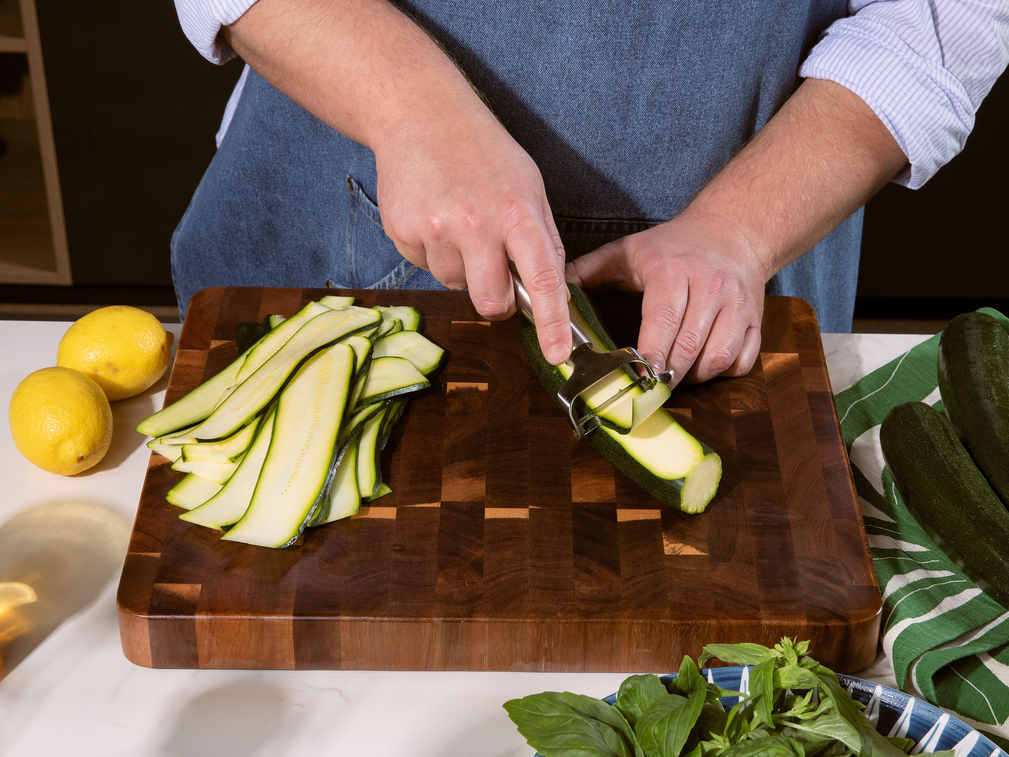 Backofen auf 220 °C Ober-/Unterhitze vorheizen. Zucchini mit einem Sparschäler oder einem scharfen Messer längs in dünne Streifen schneiden. Etwas Olivenöl in einer Grillpfanne erhitzen und die Zucchinistreifen darin portionsweise von beiden Seiten goldbraun anbraten. Herausnehmen und beiseitestellen.