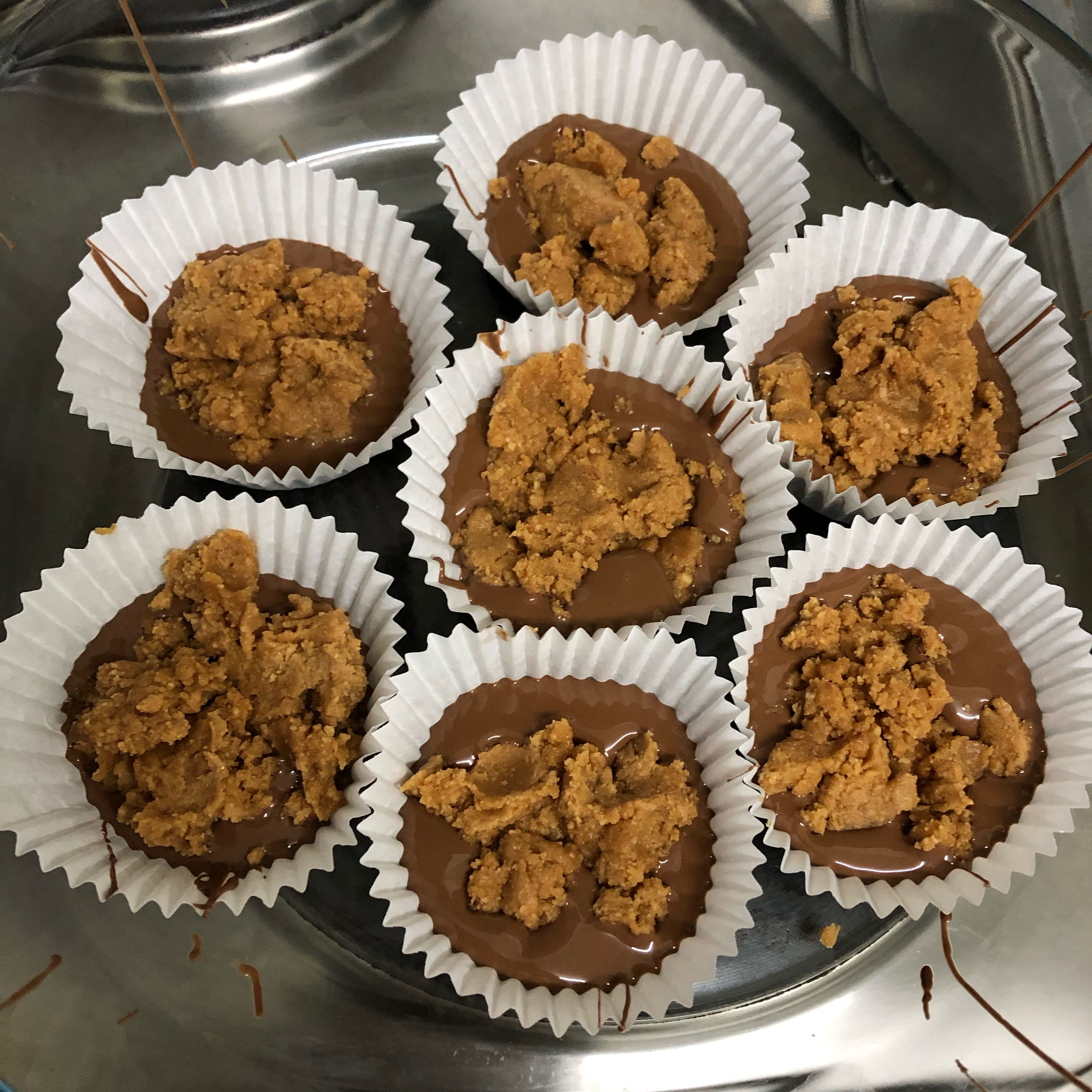 Grab a muffin tray and add your muffin paper holders. Fill it with some chocolate, add peanut butter mixture then top it off with resting chocolate. Set in fridge to rest.
