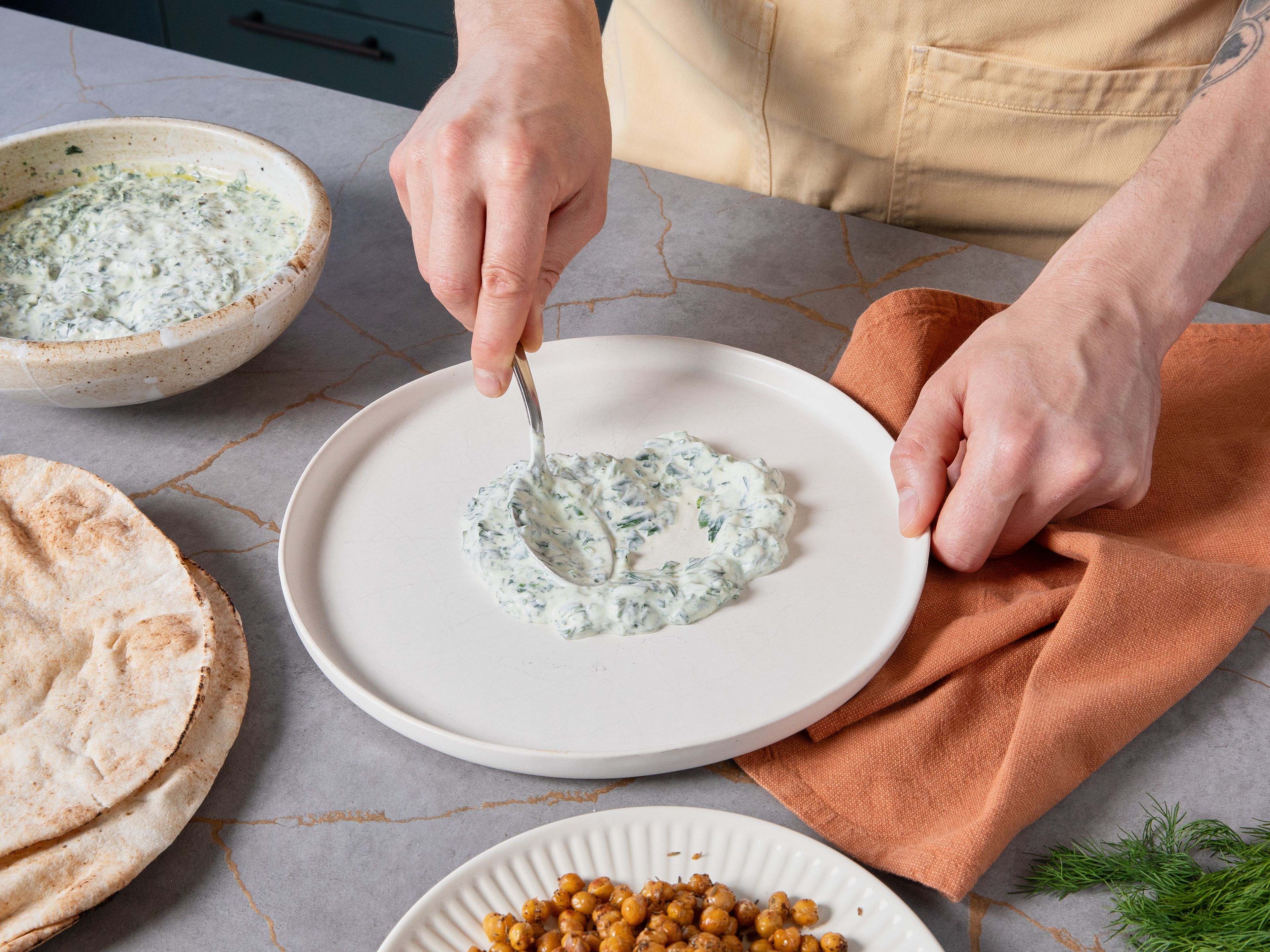 Borani auf einem großen Teller verstreichen. Das Gemüse darauf verteilen. Die knusprigen Kichererbsen darübergeben. Mit Dill bestreuen und mit restlichem Olivenöl beträufeln. Fladenbrot im Ofen oder auf dem Grill kurz erwärmen und dazu servieren.