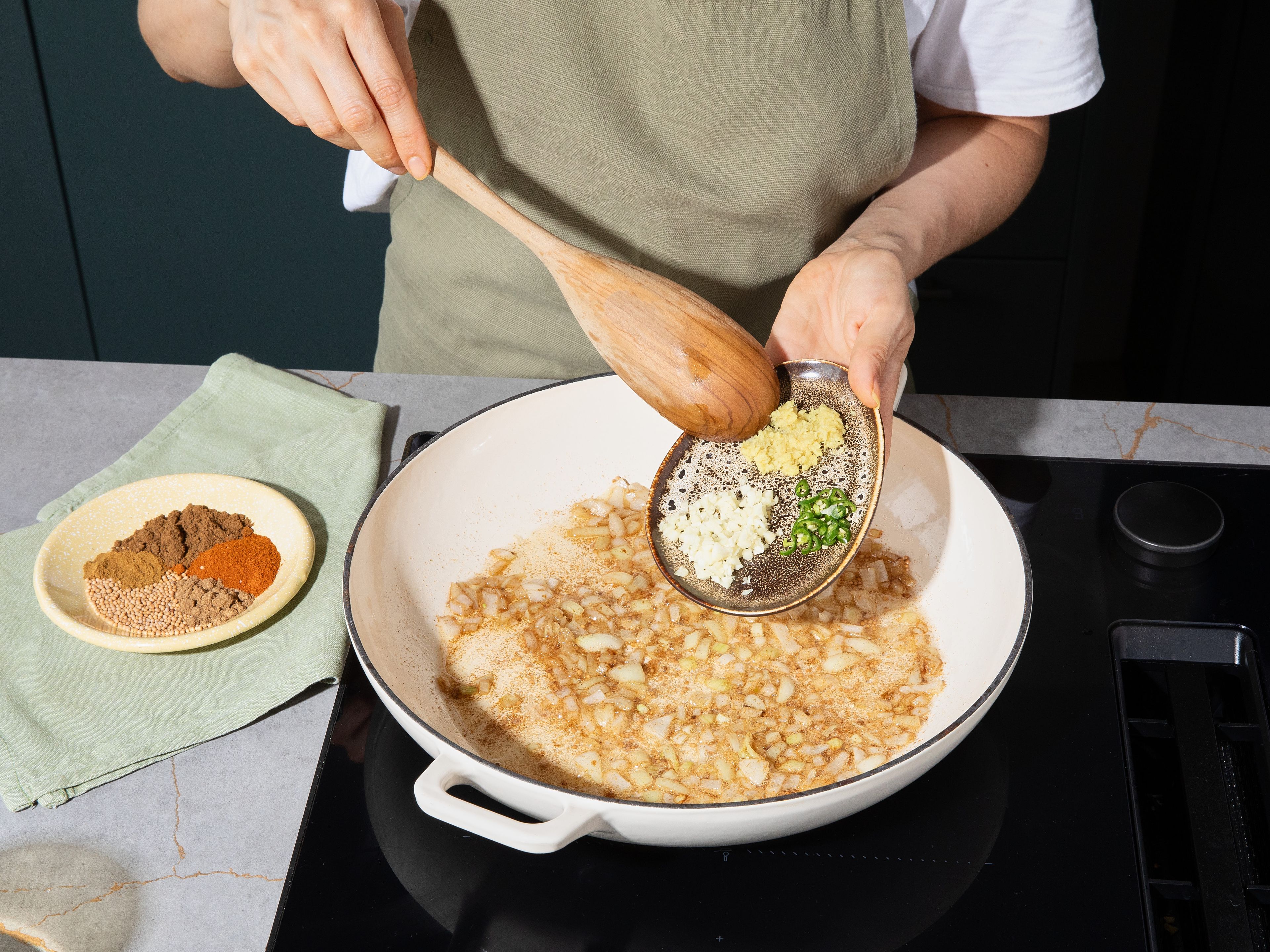 Meanwhile, for the Tadka, roughly dice onion, finely chop garlic, finely grate ginger, and cut green chili into thin rings. Heat remaining oil in a large pan. Add mustard seeds and cumin and toast until fragrant and the mustard seeds start to pop. Add onion and sauté for approx. 2–3 min. until translucent. Stir in garlic, ginger, and chili, frying for approx. 1 min. Add ground coriander, garam masala, and chili powder, roasting for approx. 2 min. Set aside about ¼ of the Tadka for garnish.