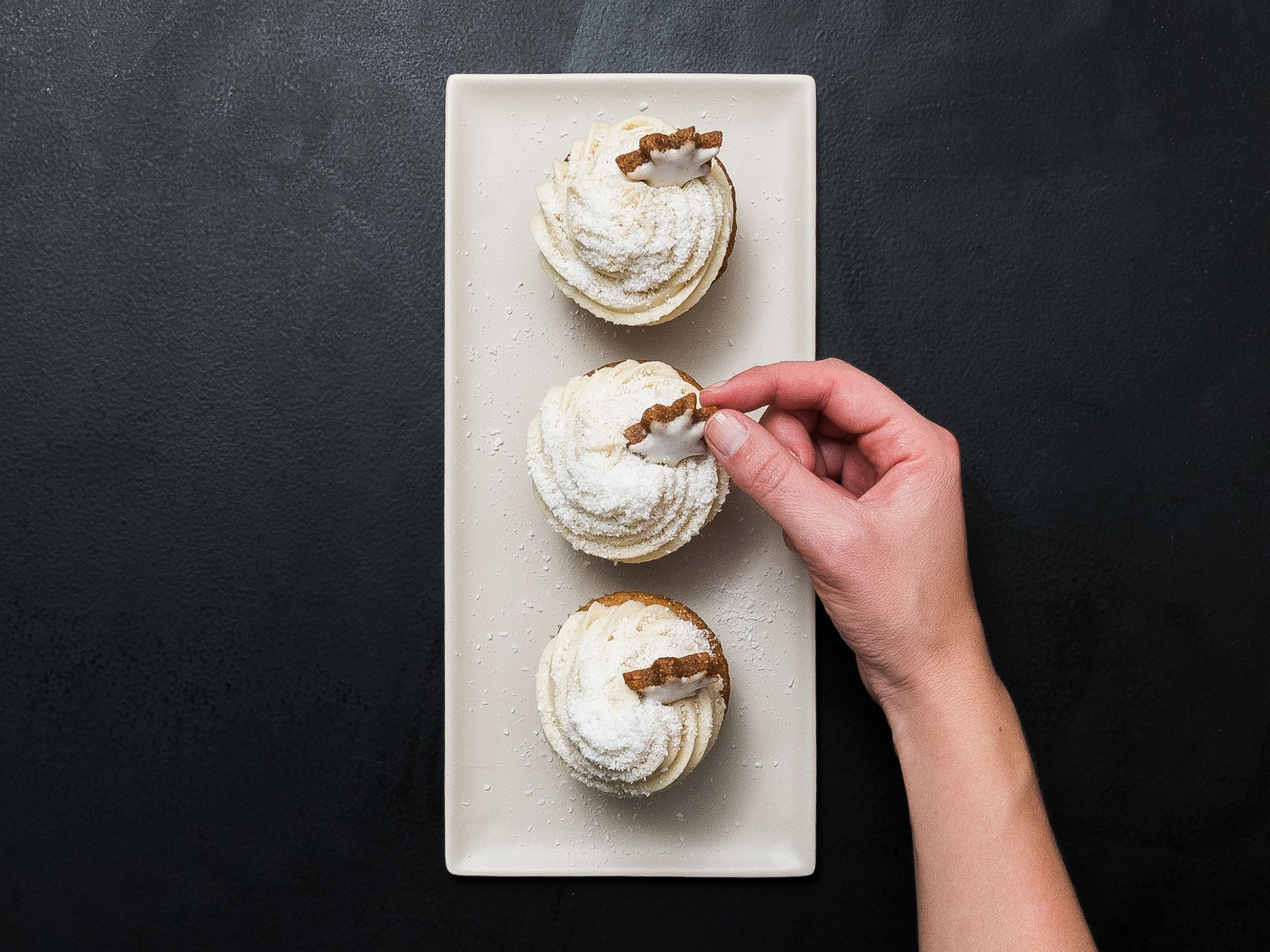 Meanwhile, for the frosting: beat butter until smooth. Add confectioner’s sugar little by little until combined. Add vanilla sugar and cream and beat until fluffy in consistency. Pipe onto cupcakes, then sprinkle shredded coconut over the cupcakes. Garnish with a cinnamon star. Enjoy!
