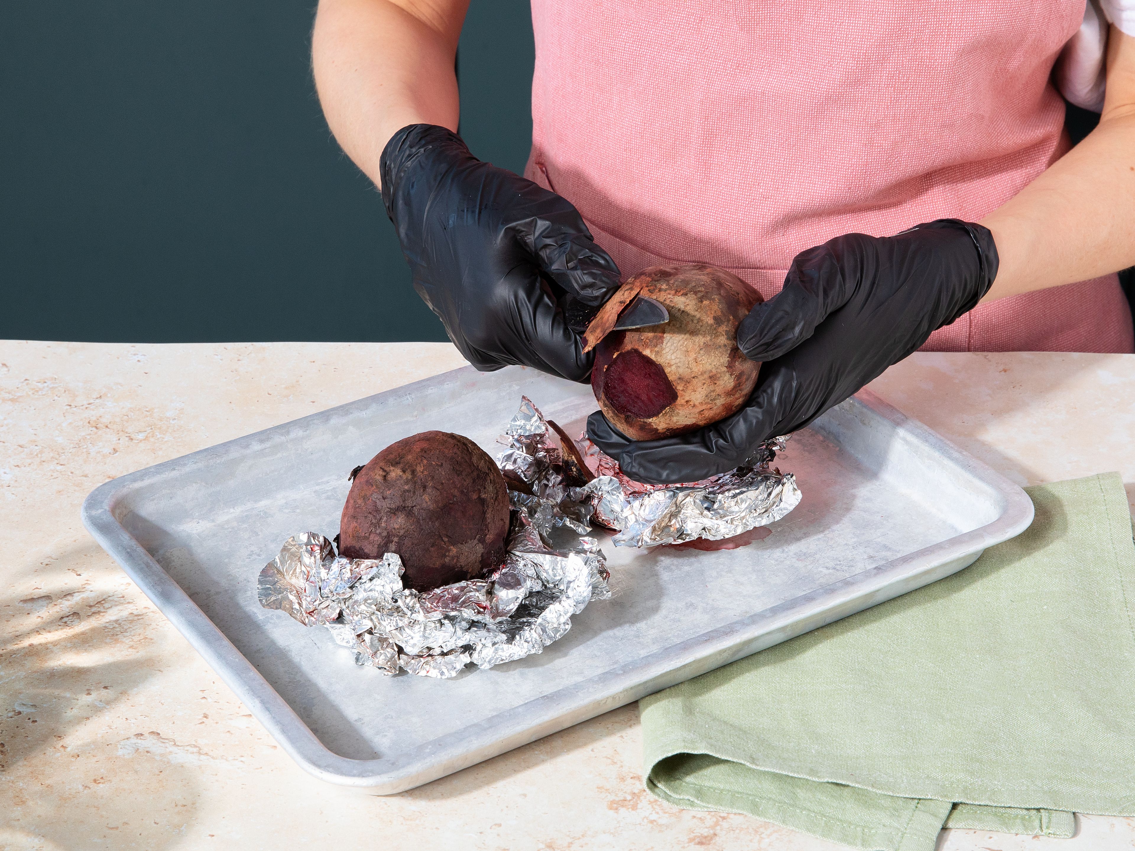 Den Backofen auf 200°C Ober-/Unterhitze vorheizen. Die Rote Bete in eine ofenfeste Form geben, etwas Wasser hinzufügen und die Form mit einem Deckel oder Alufolie verschließen. Ca. 45–50 Min. backen, bis die Rote Bete weich ist und sich leicht mit einem Messer einstechen lässt. Etwas abkühlen lassen. Anschließend nach Belieben Küchenhandschuhe anziehen, die Rote Bete schälen und grob raspeln oder fein schneiden.