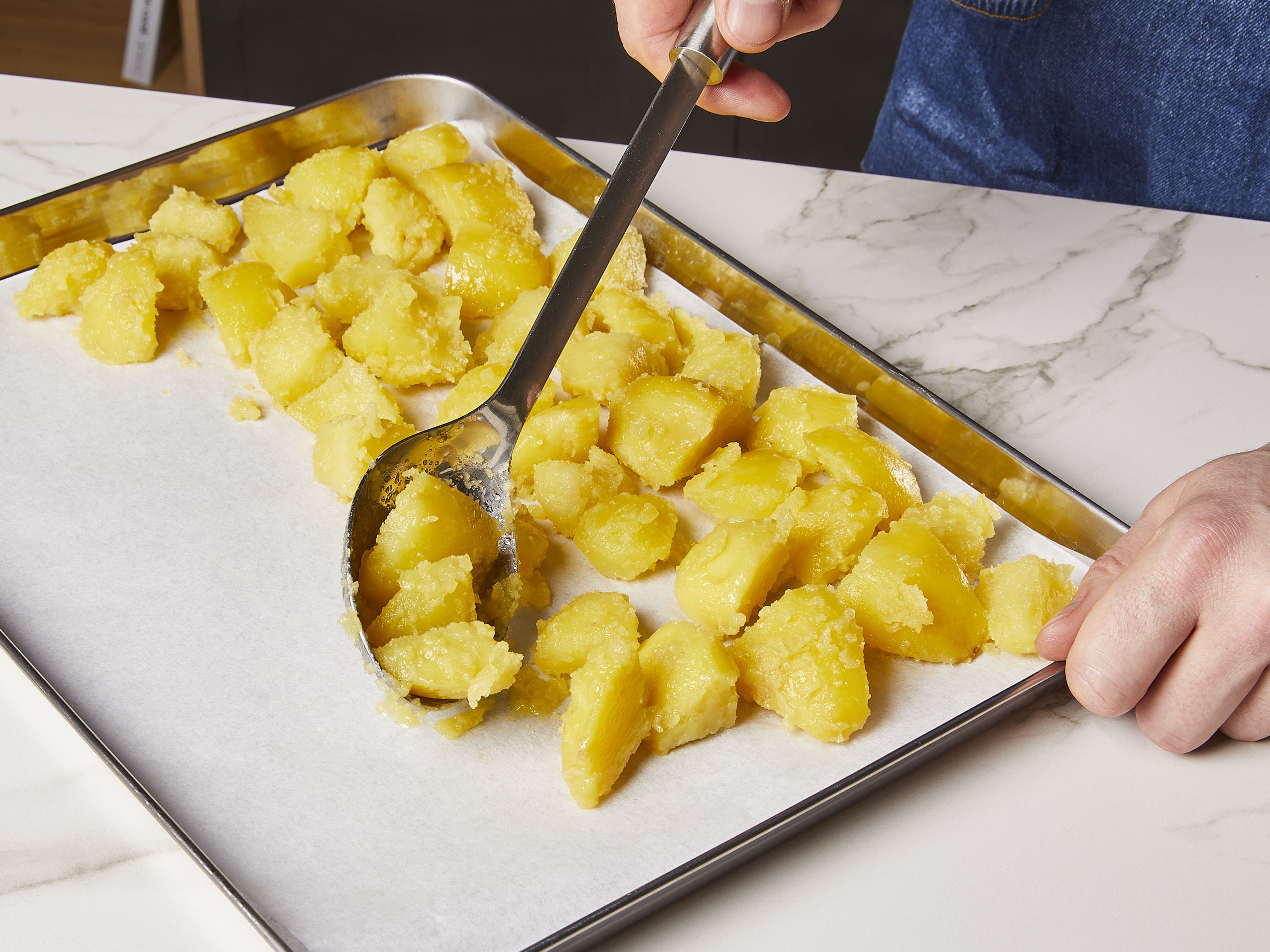 Die Kartoffeln gleichmäßig auf ein mit Backpapier ausgelegtes Backblech verteilen. In den Ofen schieben und ca. 20 Min. lang rösten, ohne sie zu bewegen. Dann mithilfe eines Pfannenwenders wenden und ca. 30 Min. weiterrösten, dabei ein paar Mal wenden, bis sie goldbraun und knusprig sind. In der Zwischenzeit die Zwiebel schälen und in dünne Streifen schneiden.