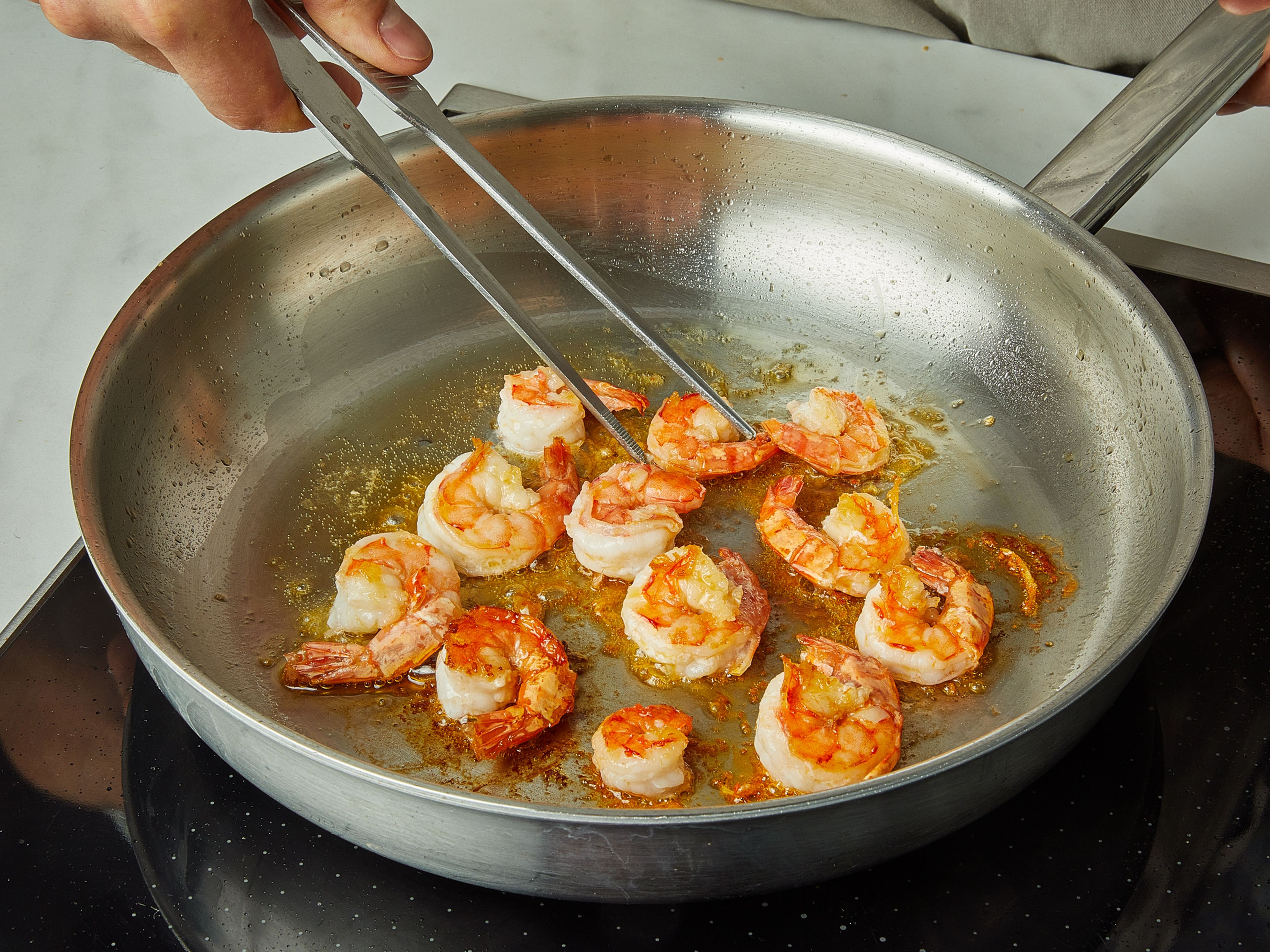 Peel and slice the garlic. Halve the cherry tomatoes. Remove the seeds from the chili and slice thinly. Heat half of the olive oil in a large pan and sear the shrimp for approx. 1 min. on each side. Remove shrimp from the pan and set it aside in a small bowl.