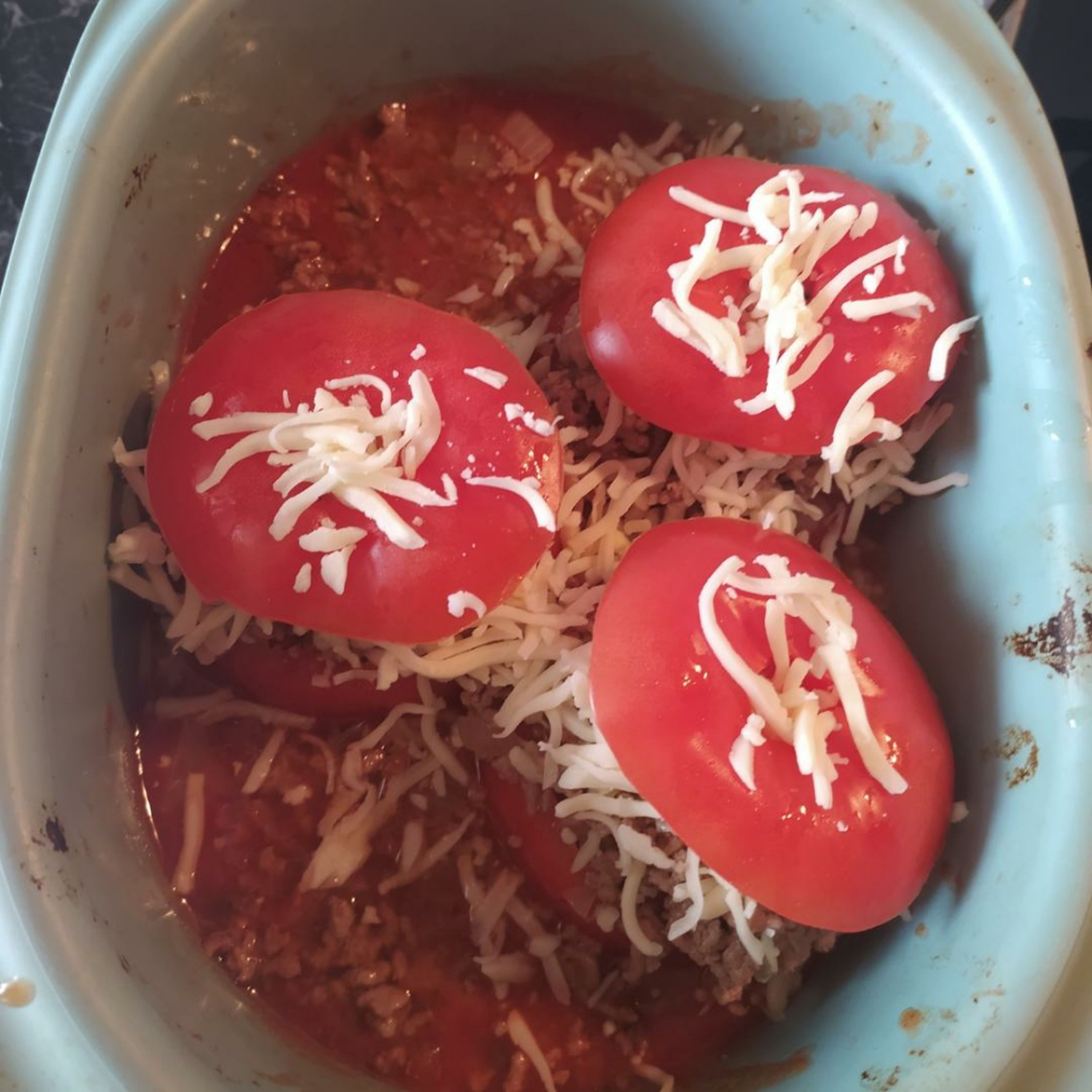 Tomaten mit Hack füllen und Brühe zugießen. Käse über die gefüllten Tomaten reiben und den Tomatendeckel wieder drauf legen. Falls du noch Hack übrig hast kannst du es mit in die Brühe geben.