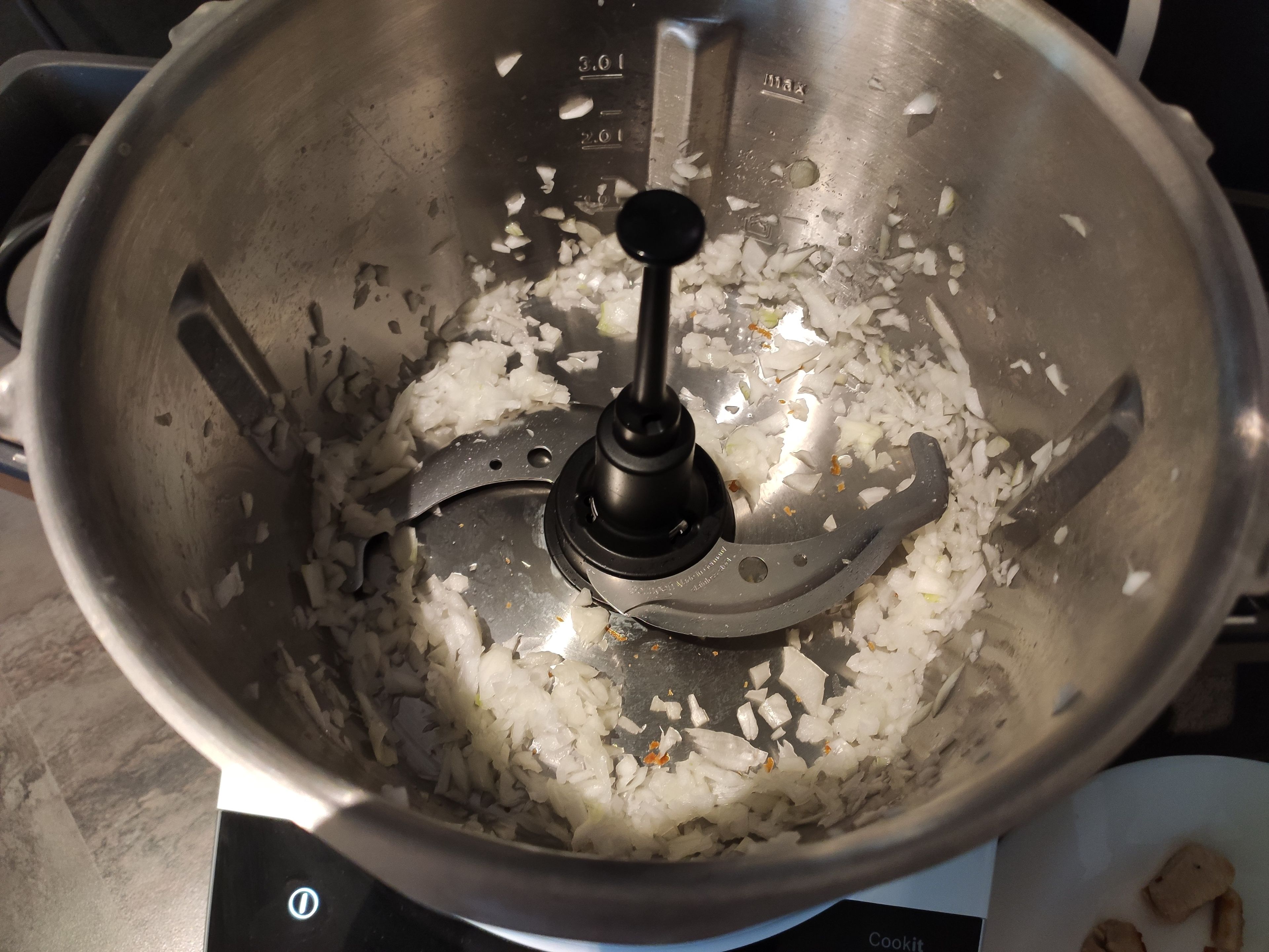 Zwiebel halbieren, in den Topf geben, den Deckel schließen, den Messerbecher einsetzen und zerkleinern (Universalmesser | Stufe 14 | 4 Sek.). Anschließend die Zwiebel mit dem Cookit-Küchenspatel nach unten schieben.