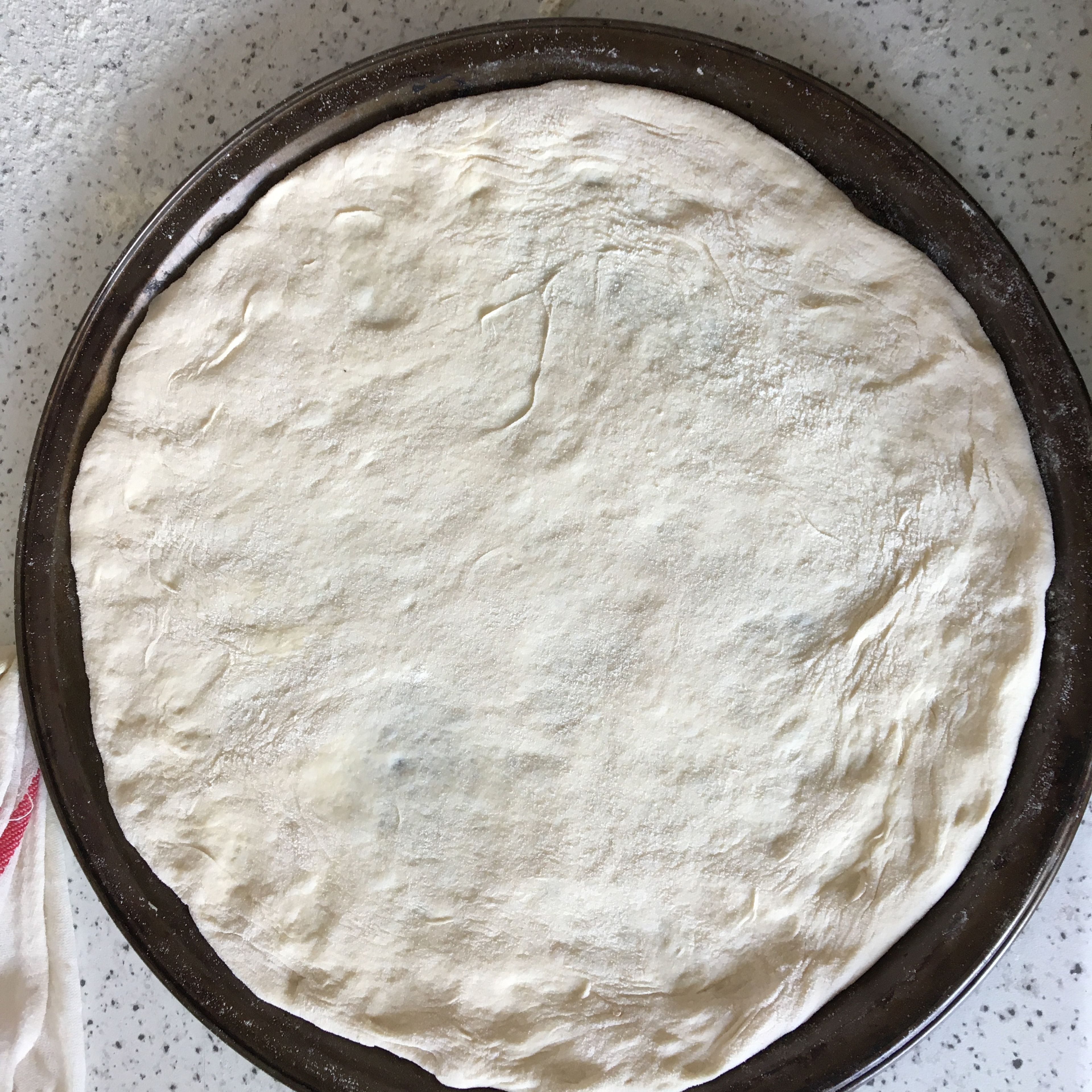 When the dough is ready, lightly grease two baking dishes. Transfer one of dough pieces onto the baking dish, letting it stretch over your hands by its own weight. Adjust into the dish and shape the rounds.