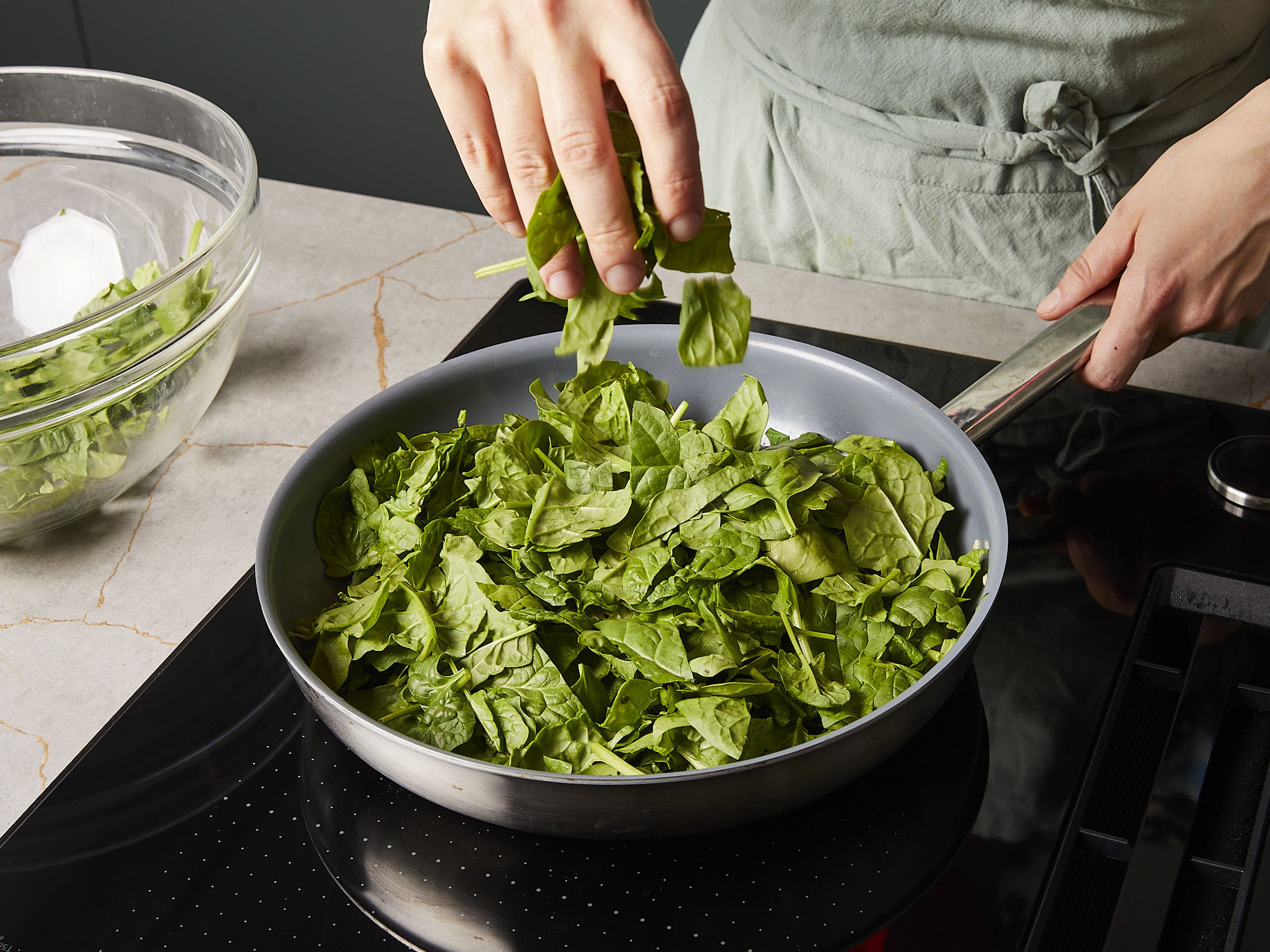 Coarsely chop spinach. Grate garlic. Heat olive oil in a pan and fry garlic for a few seconds. Add spinach and water, cover with lid and fry over medium-high heat for approx. 3–5 min. until spinach starts to wilt.