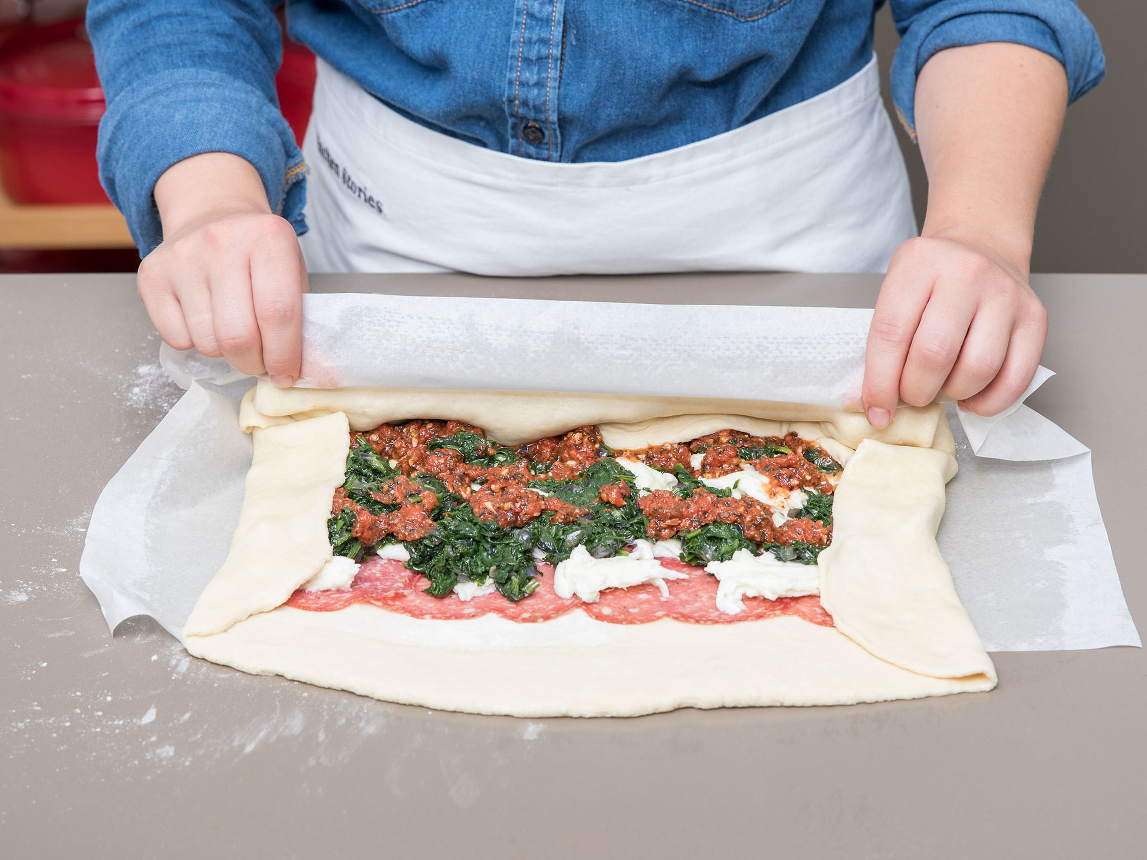 Preheat oven to 180°C/350°F. Brush a sheet of parchment paper with some olive oil. Flour a working surface and roll dough out into a rectangle. Transfer the dough onto the parchment paper. Layer on slices of fennel salami, followed by the prosciutto, leaving approx. a 3-cm/1-in border around the edge. Tear mozzarella and place on top, spoon on the cooked spinach, followed by the tomato sauce. Pick up the the  side of the parchment paper closest to you, lift it up and fold over, rolling the dough into a tight log. Pinch along the seam and tuck in the ends.