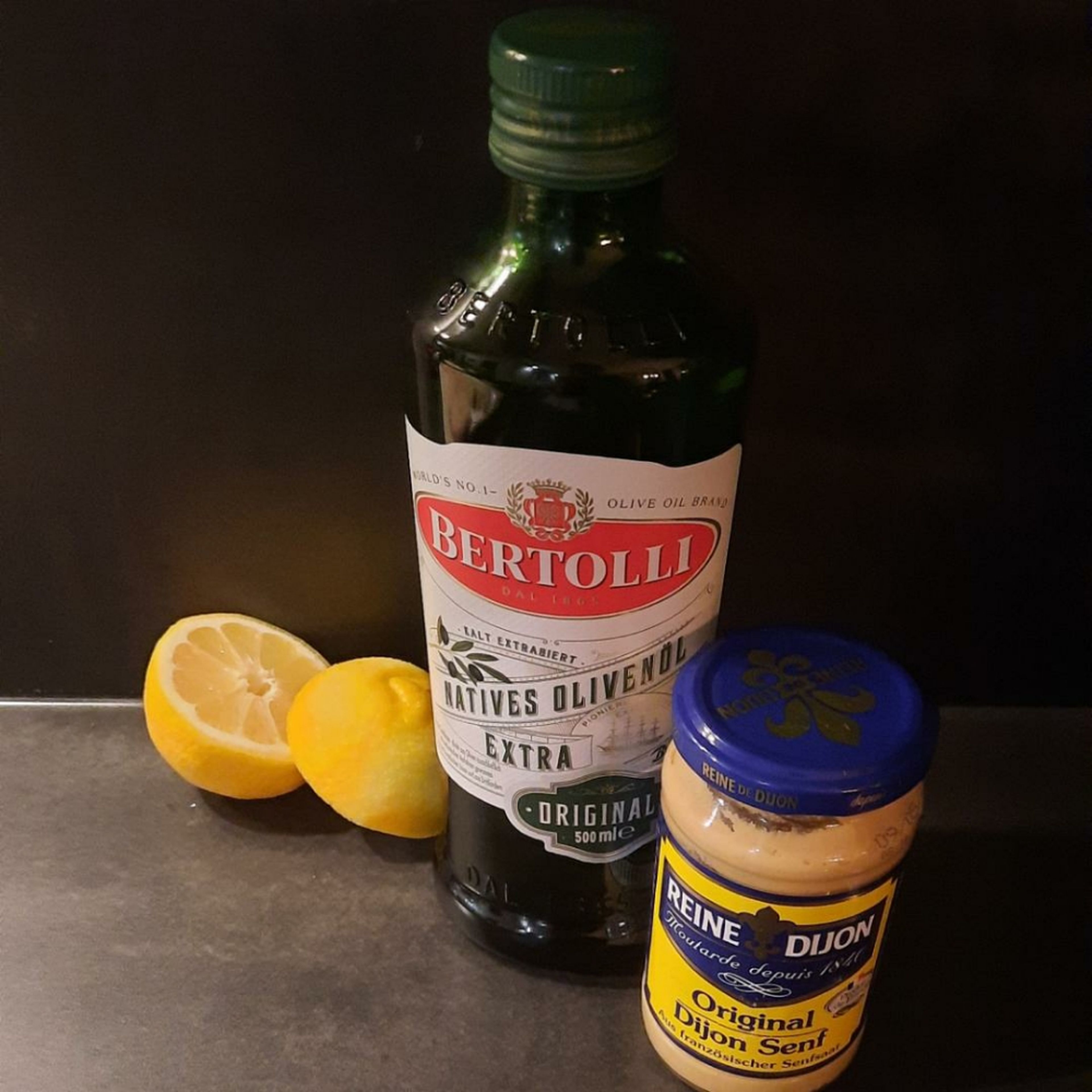 Zitronensaft mit dem Olivenöl und dem Senf verrühren. Den Abrieb hinzugeben.