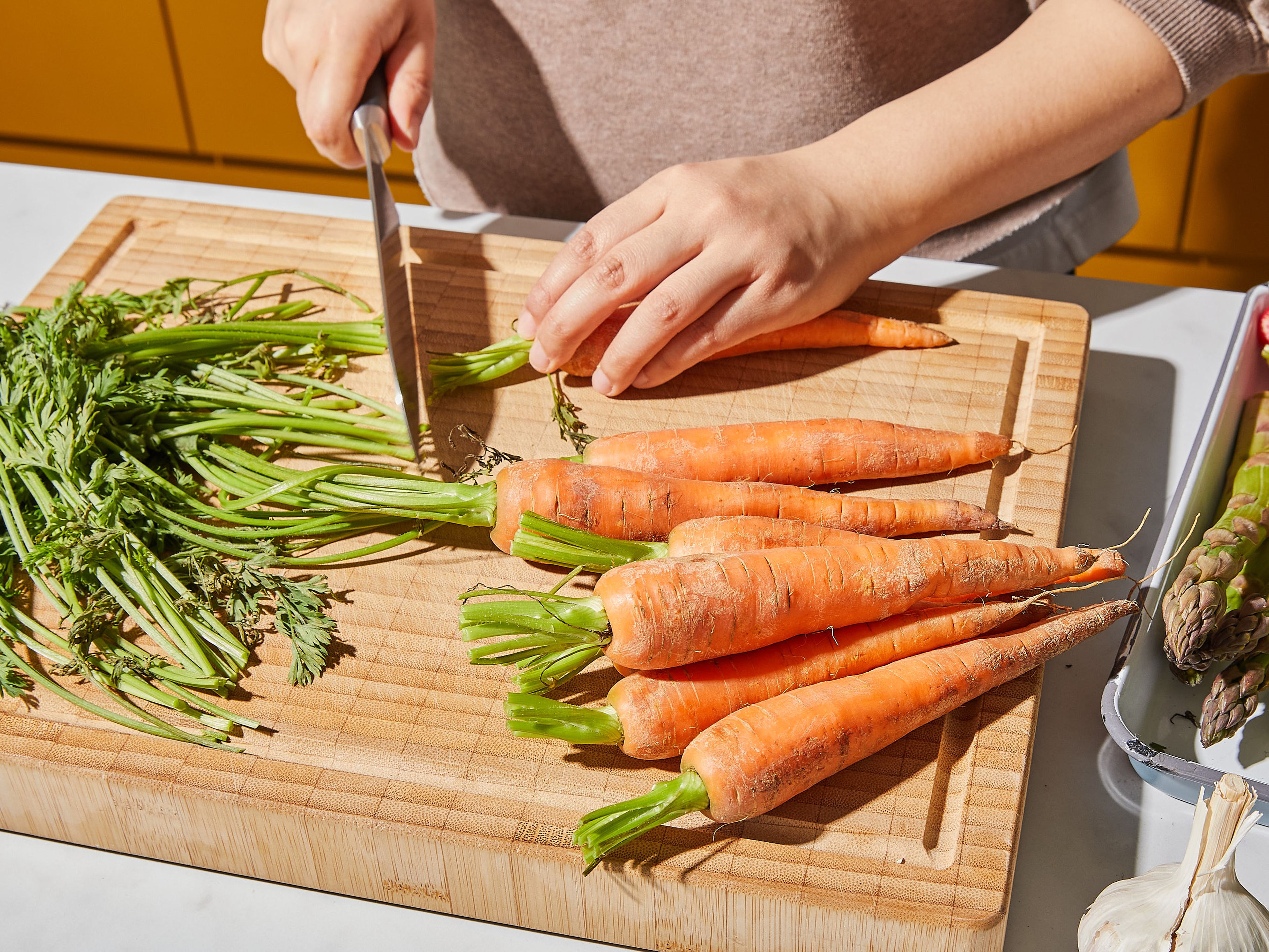 Den Backofen auf 180°C vorheizen. Das Karottengrün auf ca. 2 cm kürzen, falls du Karotten mit Grün verwendest. Die Knoblauchknolle der Länge nach halbieren. Die holzigen Enden des Spargels entfernen. Das Grün der Radieschen ebenfalls entfernen und Frühlingszwiebeln von den Wurzelenden befreien.