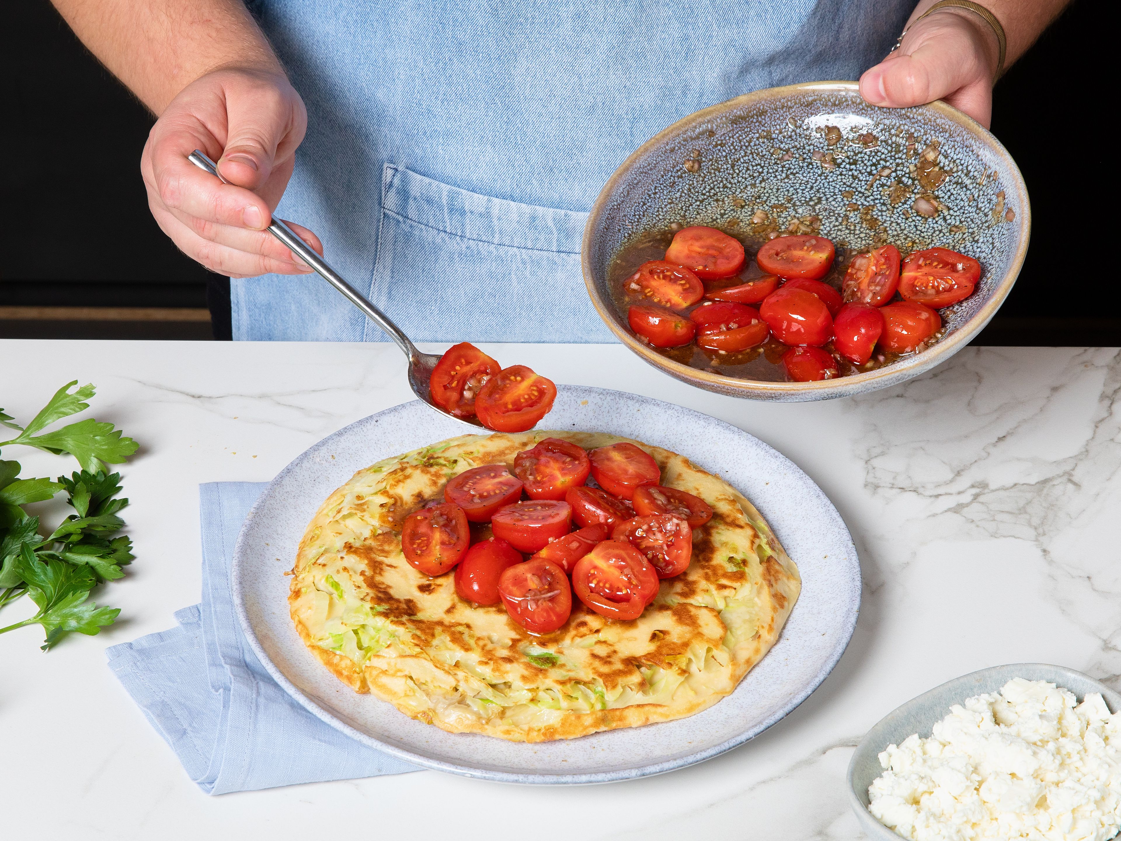 Fertige Pfannkuchen auf Teller legen. Tomatensalat darauf anrichten, Feta darüber bröseln und mit gehackter Petersilie garnieren.