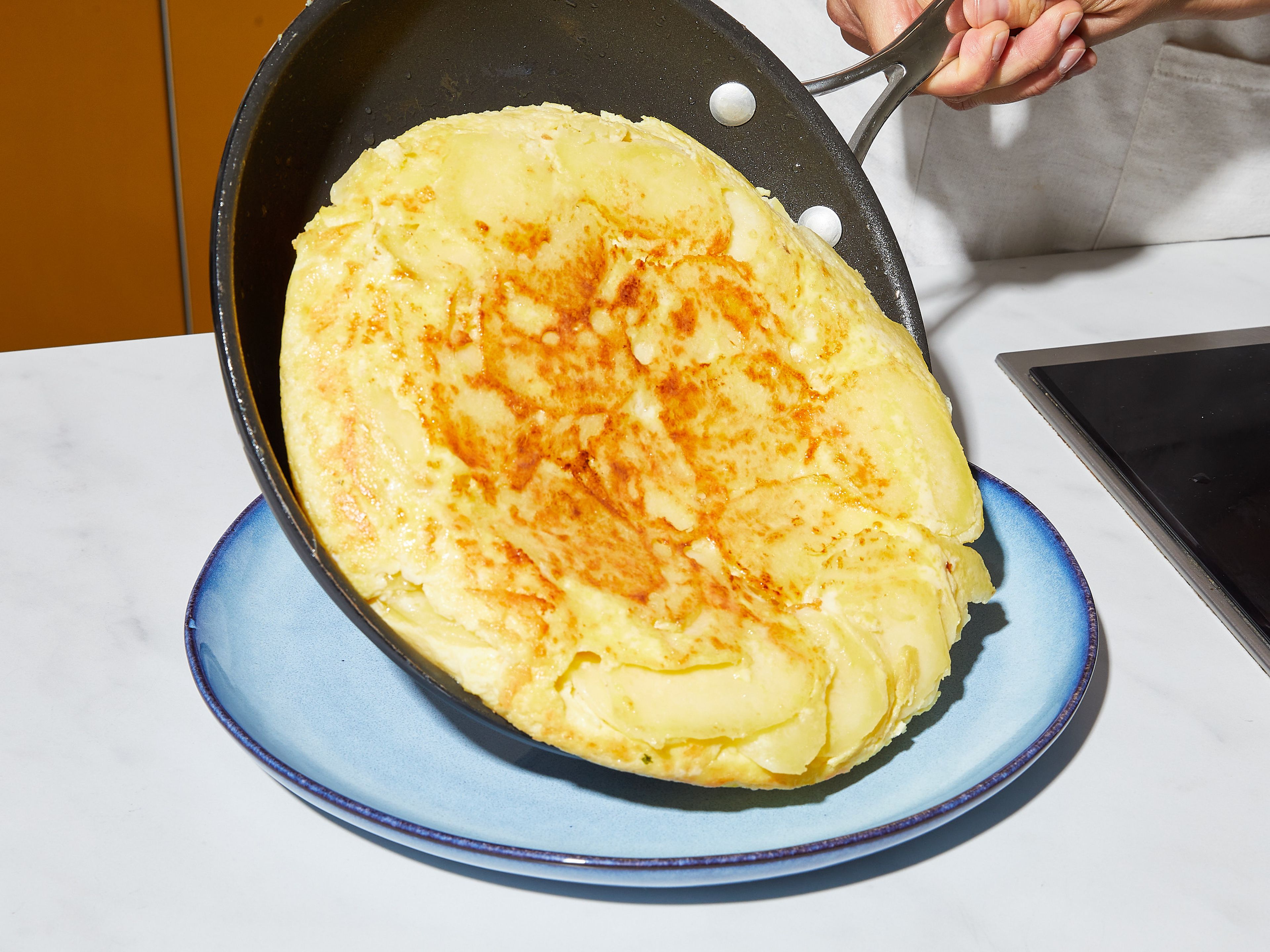 Dieselbe Pfanne auf mittlerer Stufe erhitzen und 3 EL Öl, sowie die Ei-Kartoffel-Mischung hineingeben. Glattstreichen und in der Pfanne ca. 15 – 20 Min. stocken lassen, bis die Eier fast fest sind, die Oberfläche aber noch leicht flüssig ist. Die Tortilla mit Hilfe eines großen Tellers vorsichtig stürzen und mit der gebräunten Seite nach oben zurück in die Pfanne gleiten lassen. Weitere 5 Min. braten, dann auf einen großen Teller gleiten lassen. Wie einen Kuchen aufschneiden und servieren. Guten Appetit!