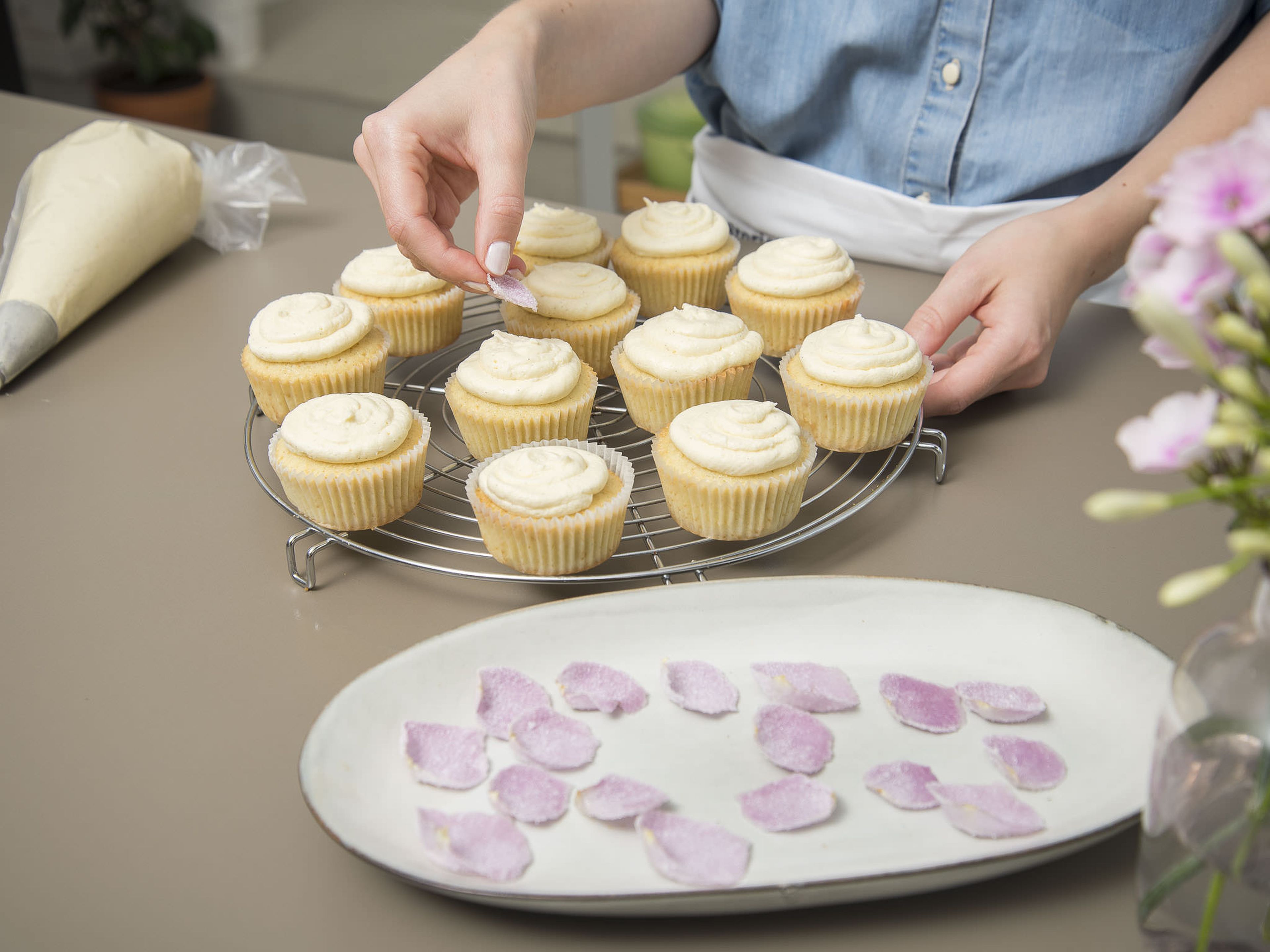 Frost the cupcakes by working your way from inside out, drawing upwards in circles. Decorate each cupcake with a sugarcoated rose petal. Enjoy!