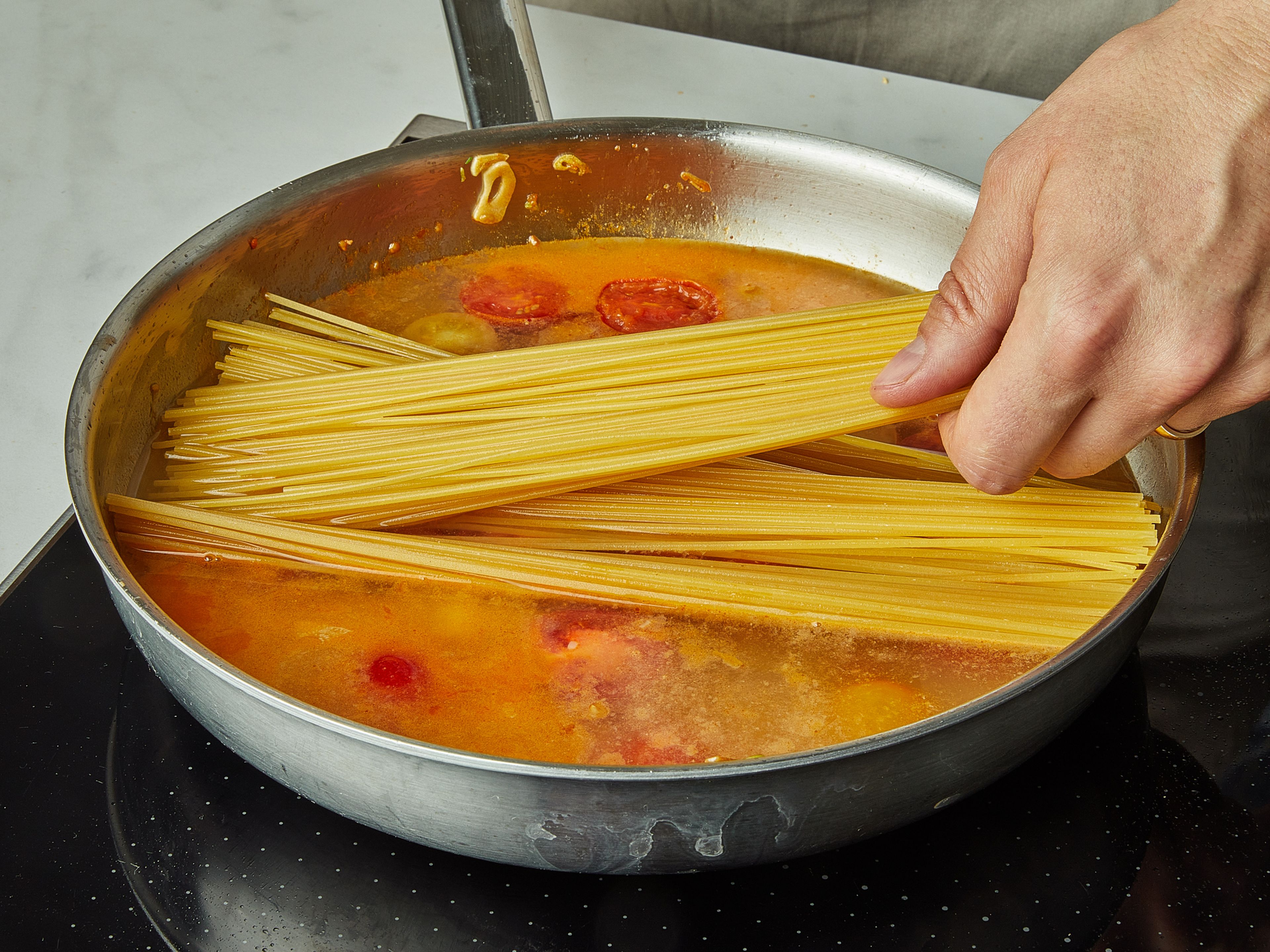Die Spaghetti auf die Mischung in der Pfanne geben und das Wasser hinzufügen. Die Nudeln sollten vollständig mit Wasser bedeckt sein. Das Wasser mit Salz würzen. Den Deckel aufsetzen und ca. 9 Min. köcheln lassen. Nach ein paar Minuten alles umrühren, damit es nicht zusammenklebt, ggf. mehr Salz hinzufügen.
