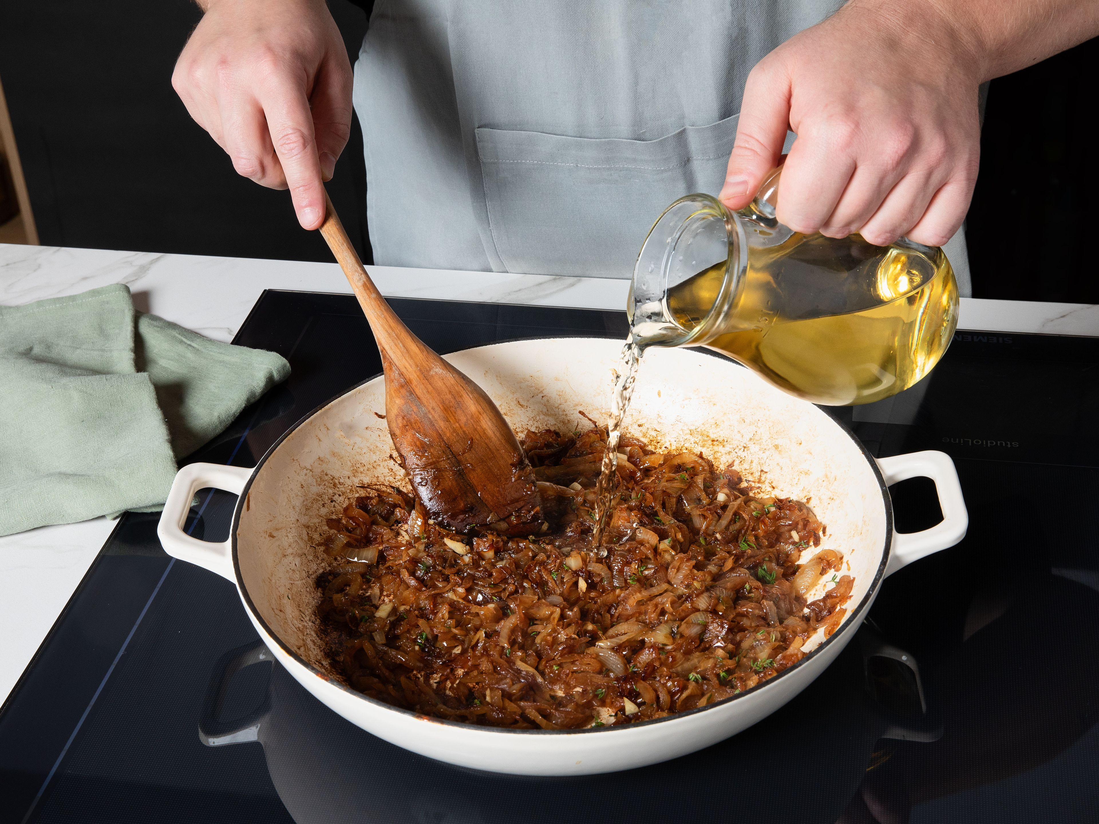 Sobald die Zwiebeln sehr weich und goldbraun karamellisiert sind, mit Weißwein ablöschen. Dabei mit einem Holzlöffel die braunen Röstaromen vom Pfannenboden lösen. Dann Thymianzweige und den gehackten Knoblauch hinzufügen, einrühren und alles ca. 2–3 Min. köcheln lassen, bis sich ein intensiver Duft entfaltet.