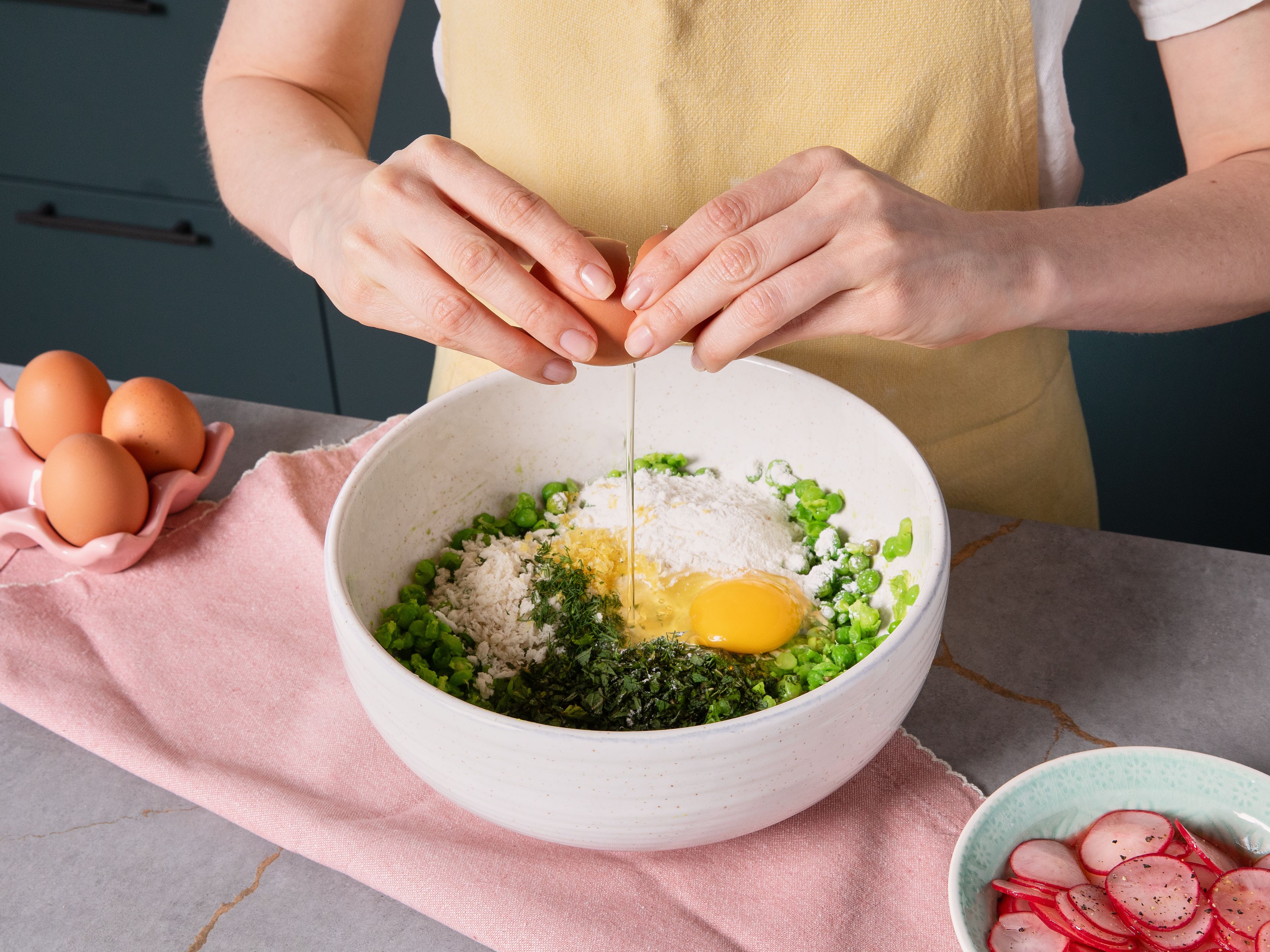 Die aufgetauten Erbsen in einer großen Schüssel mit einer Gabel zerdrücken. Ei, Mehl, Backpulver, Zitronenabrieb, Knoblauch, Minze, Dill und Panko dazugeben. Alles zu einer klebrigen Masse vermengen und mit Salz und Pfeffer würzen. Bei Bedarf etwas mehr Panko oder Mehl untermischen.