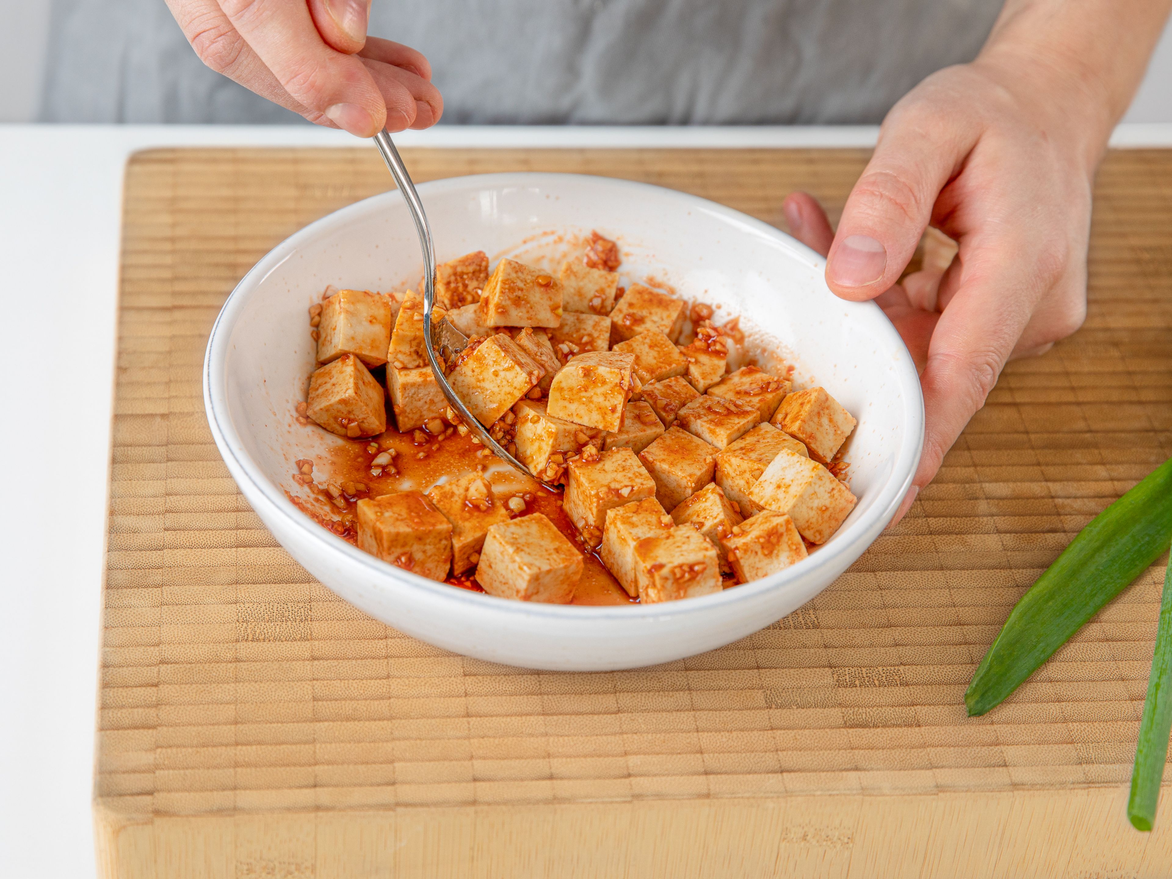 Für die Tofu-Marinade, Knoblauch und Ingwer schälen und beides fein hacken. Sojasauce, Gochujang, Knoblauch, Ingwer und die Hälfte des Zuckers in einer Schüssel verrühren. Tofu in mundgerechte Würfel schneiden, in die Marinade geben und gut vermischen. Für ca. 10 Min. marinieren lassen.