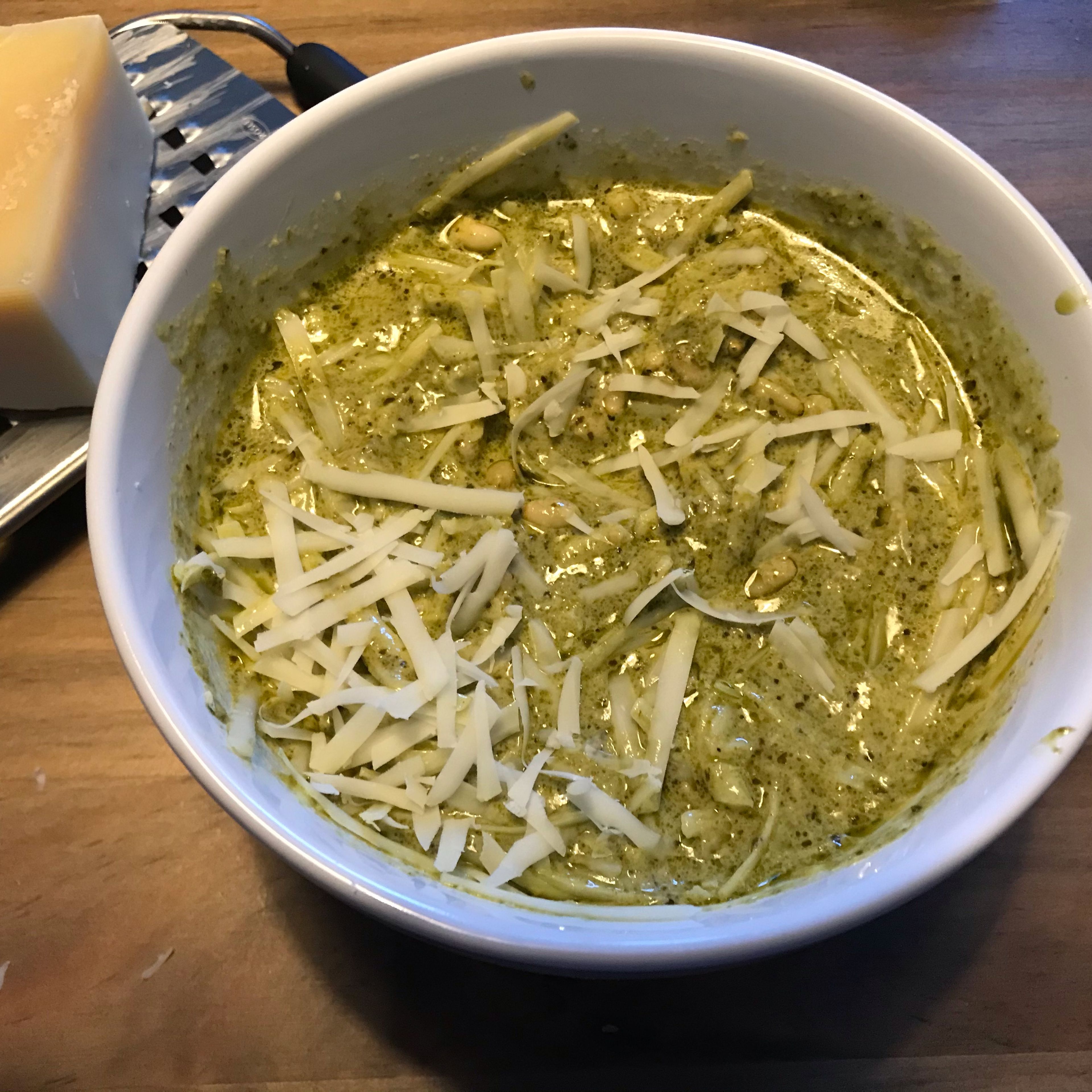 In a small bowl, add pesto, pine nuts and cream. Grate half of the cheese over the pesto and mix well.