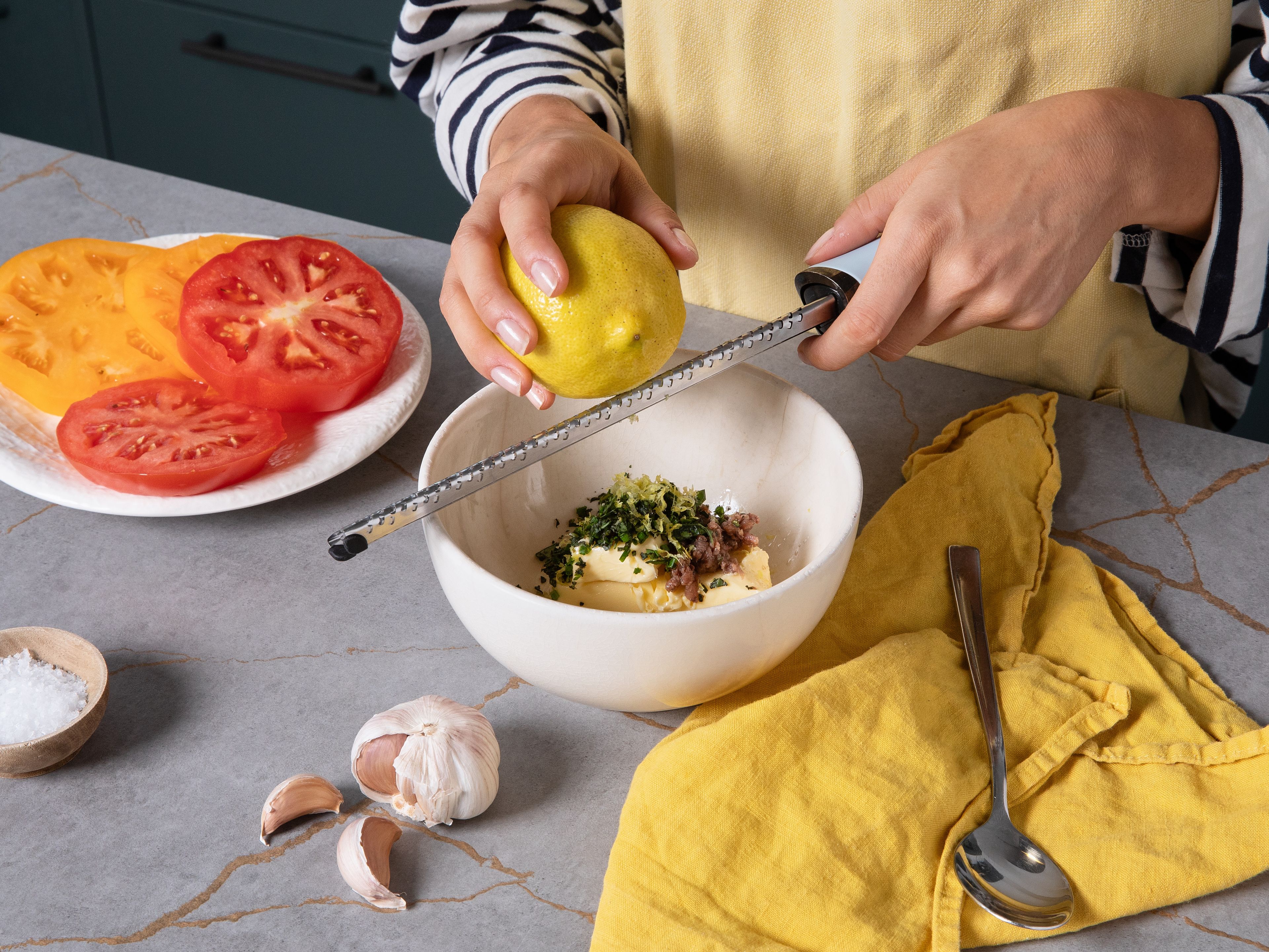 Finely chop the herbs and anchovies, grate the garlic, and zest and juice the lemon. Add everything to a bowl with the butter, salt, and pepper, and stir until smooth. Trim the tops and bottoms of the tomatoes and set aside for another use. Slice the tomatoes into thick rounds.