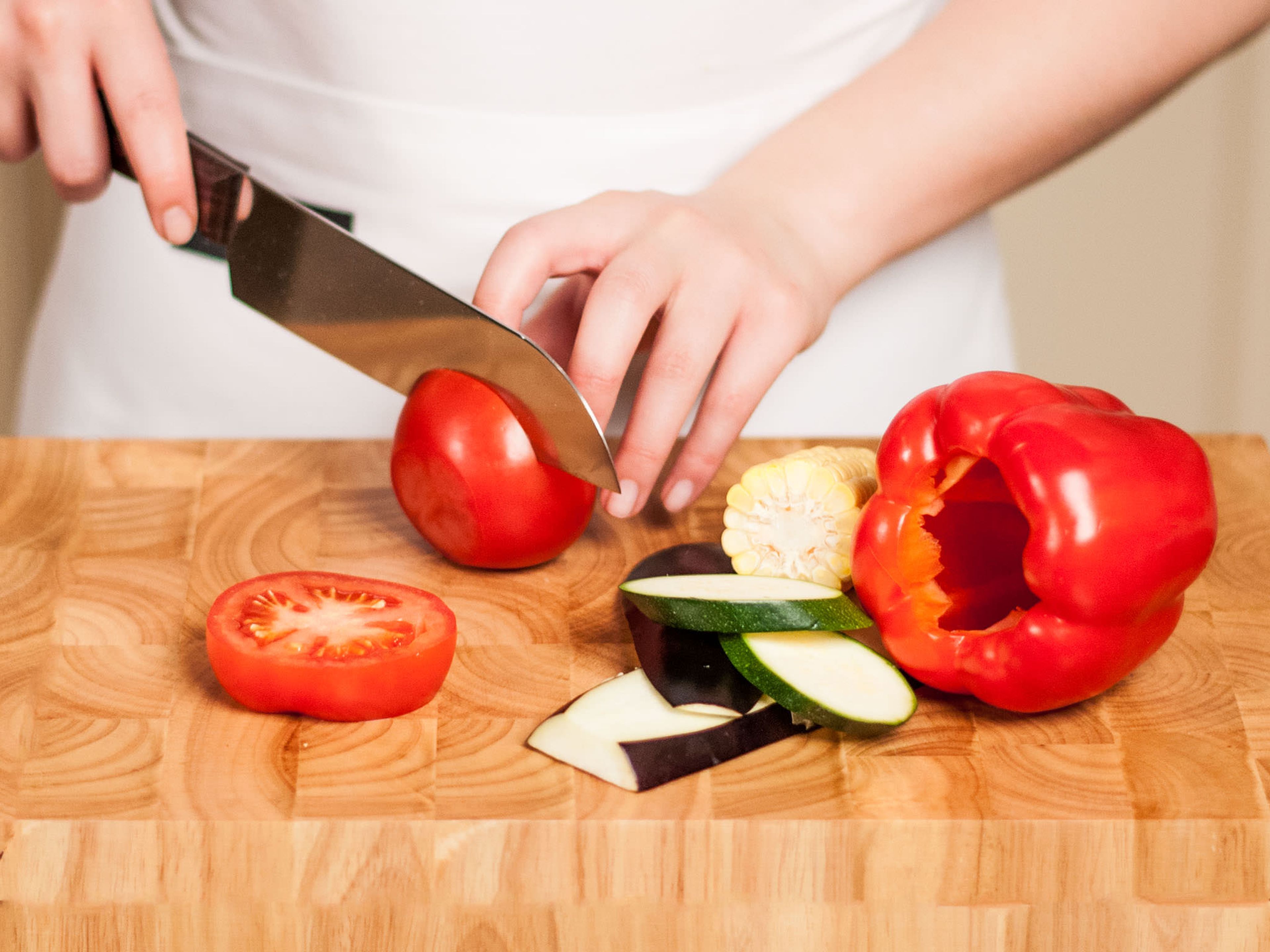 Den Deckel der Paprika abschneiden und würfeln. Das Kerngehäuse entfernen. Tomate, Zucchini und Aubergine in dicke Scheiben schneiden und jeweils den Strunk entfernen.