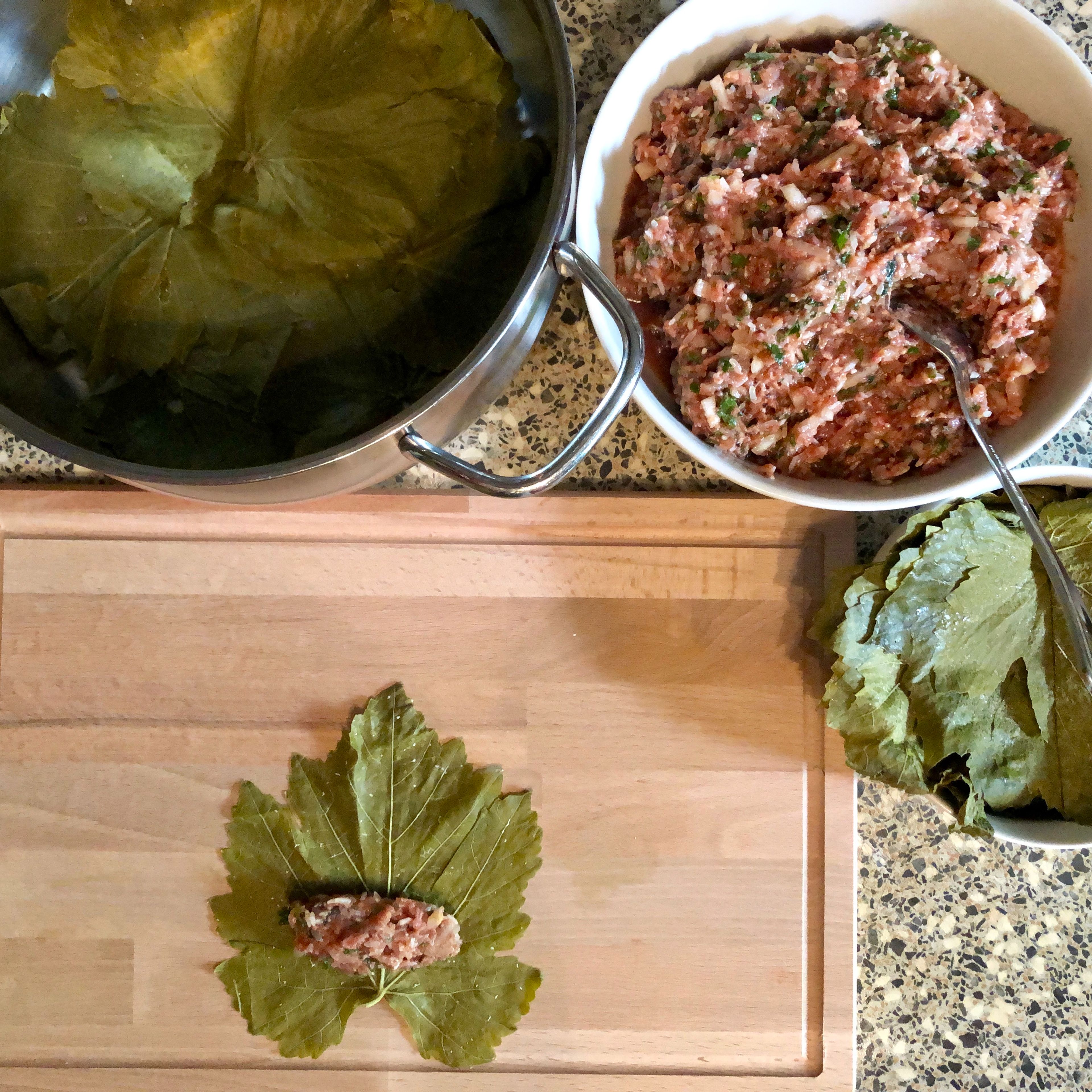 Now the fun part. Spread a leaf on a plate or cutting board, wrong side up and stem end towards you. Put a teaspoon of filling near the stem end. With your hands fold the sides and then roll up like a cigar.
