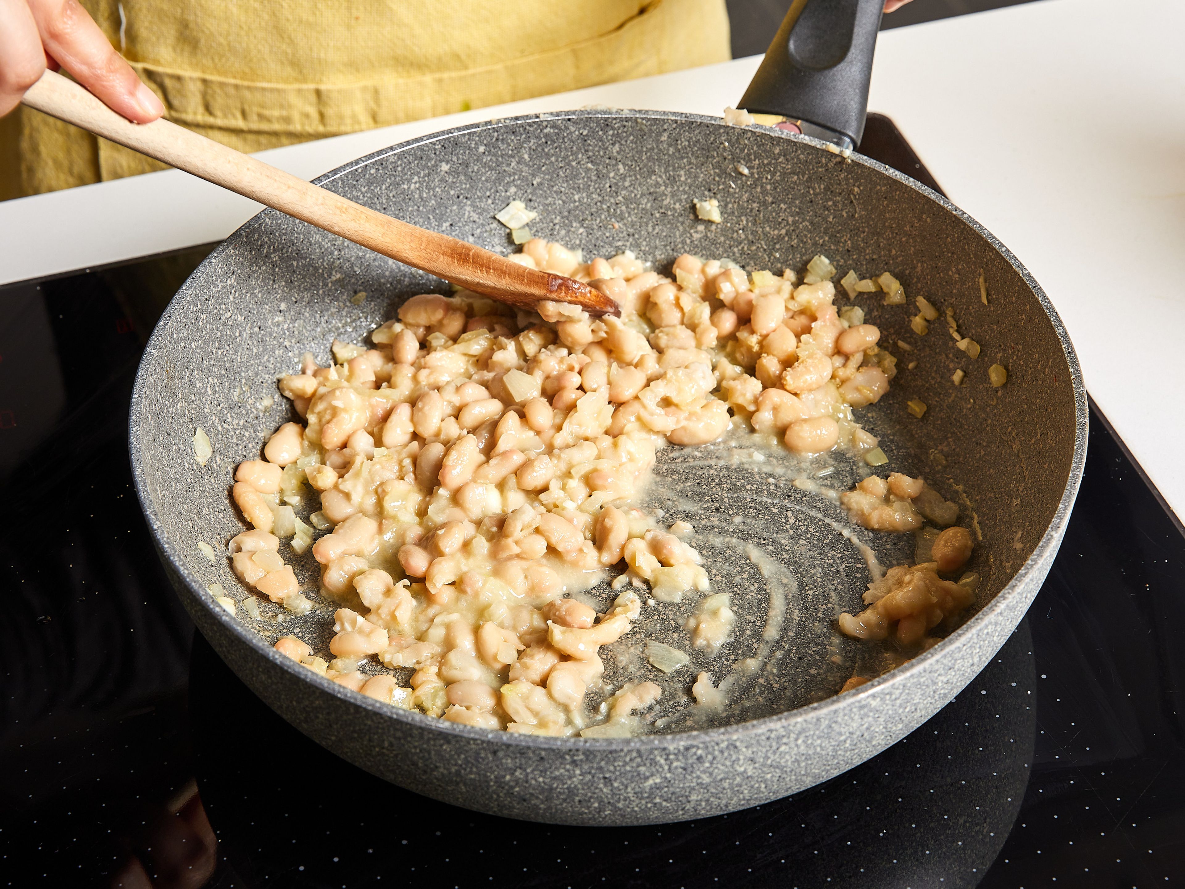 Die Bratpfanne mit etwas Küchenpapier auswischen. Das restliche Olivenöl hinzufügen und bei mittlerer Temperatur erhitzen. Zwiebeln hinzufügen und glasig dünsten. Dann den Knoblauch hinzugeben und kurz anbraten. Weiße Bohnen dazugeben und ca. 3 Min. anbraten. Dann die Hefeflocken und einen Teil des aufbewahrten Nudelwassers hinzufügen. Mit dem Pfannenwender oder einer Gabel die weißen Bohnen zerdrücken. Während des Prozesses weiteres Nudelwasser hinzugeben, bis die Soße cremig ist.