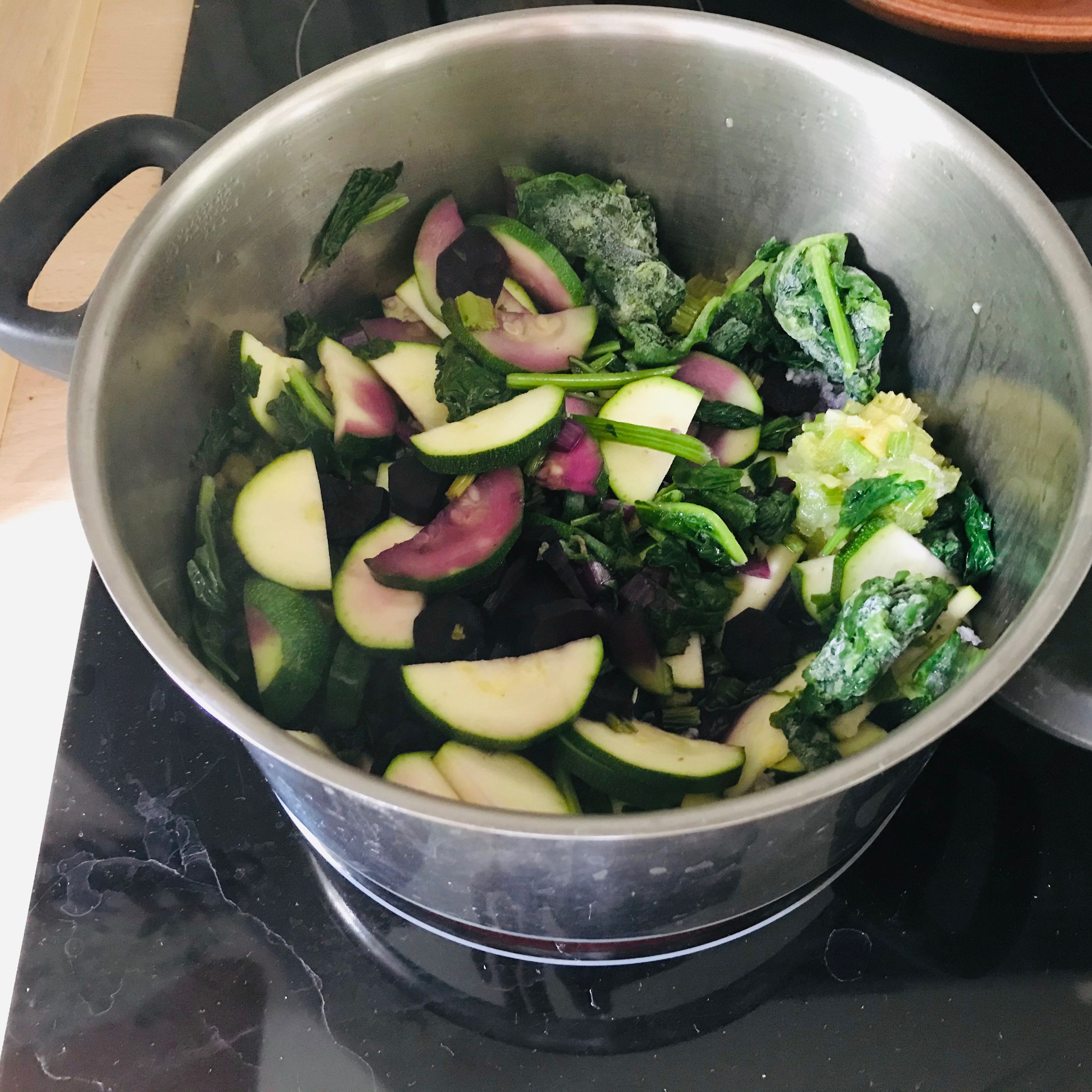Geschnittene Zucchini, Karotte, Staudensellerie, Knoblauch sowie den Spinat zu den Zwiebeln geben und köcheln lassen, bis das Wasser aus dem Gemüse verdunstet ist.