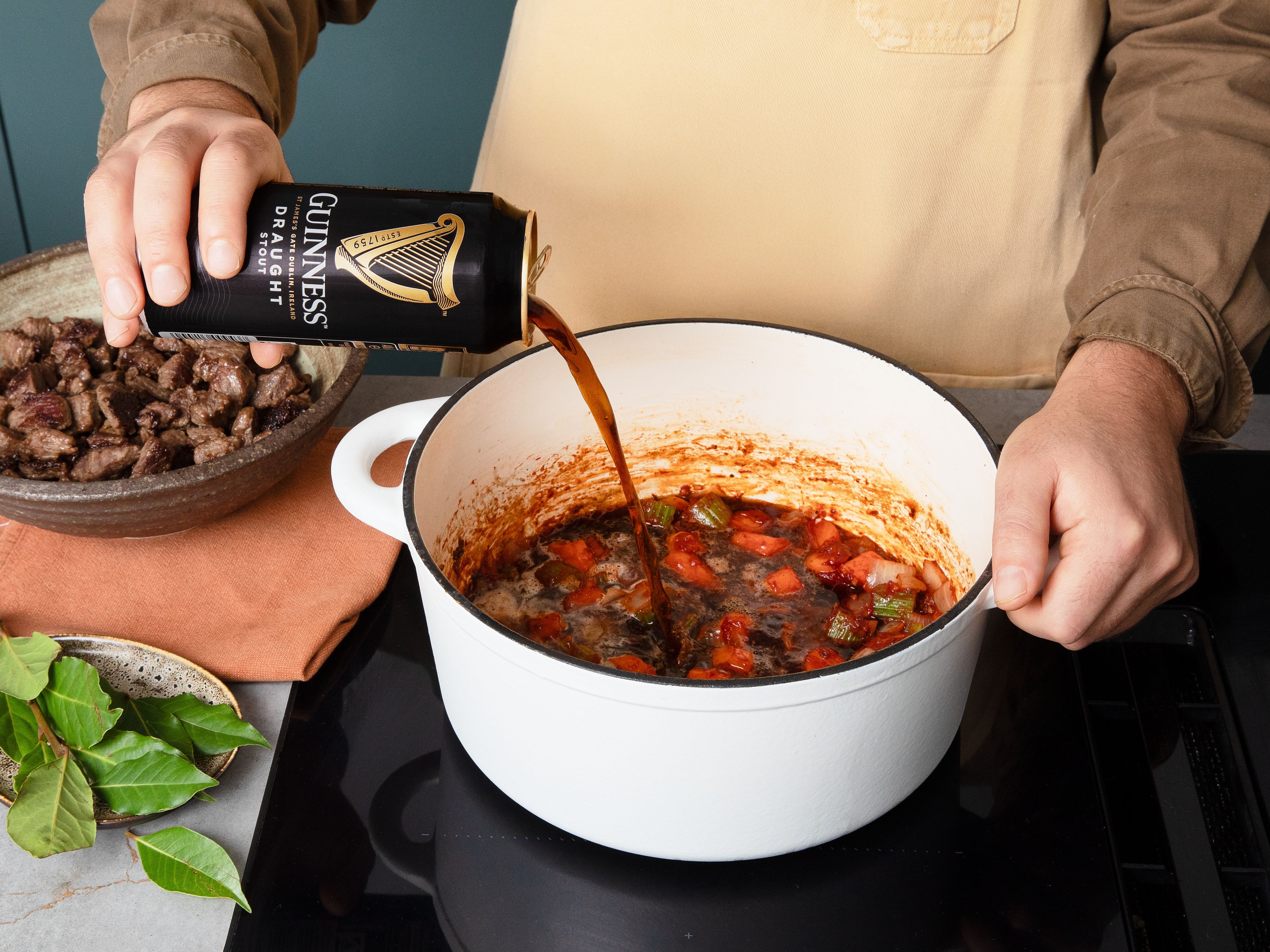 Die Hitze etwas reduzieren. Dann im Bratensatz die Zwiebeln, Karotten und Sellerie ca. 5 Min. anbraten, bis sie leicht gebräunt sind und mit Salz und Pfeffer würzen. Die Hälfte des Knoblauchs hinzufügen und ca. 30 Sek. kurz mitrösten, dann Tomatenmark zugeben und ca. 2–3 Min. karamellisieren lassen. Mit Guinness Draught und Brühe ablöschen, dabei die Röststoffe vom Topfboden lösen. Fleisch samt Bratensaft zurückgeben, Lorbeerblätter hinzugeben, gut umrühren und bei niedriger Hitze abgedeckt ca. 1 Std. sanft schmoren lassen. Währenddessen mit dem Rezept fortfahren.