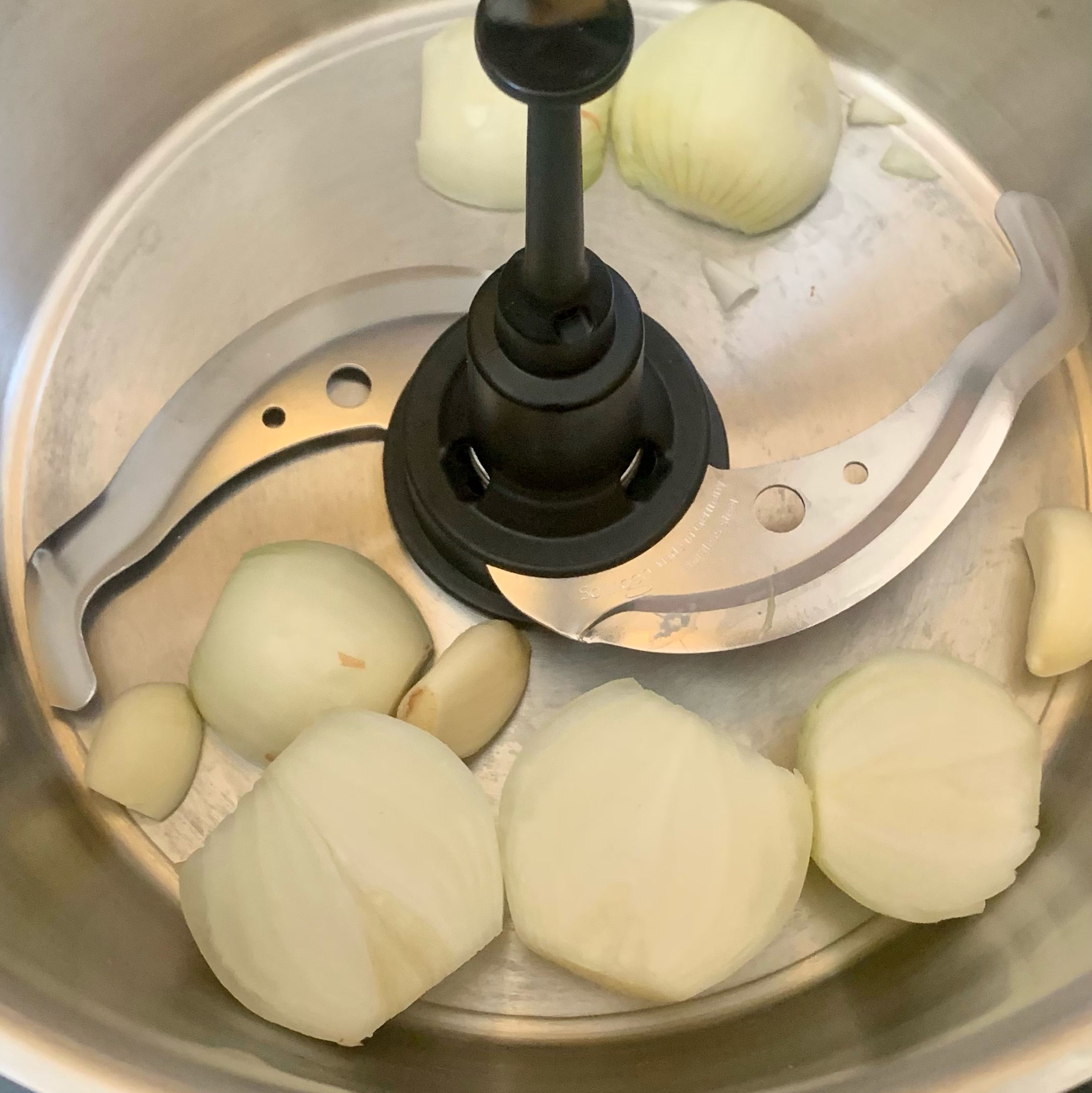 Universalmesser einsetzen und Zwiebeln und Knoblauch in den Cookit geben. Im manuellen Kochen 10 Sekunden bei Stufe 15 alles zerkleinern.