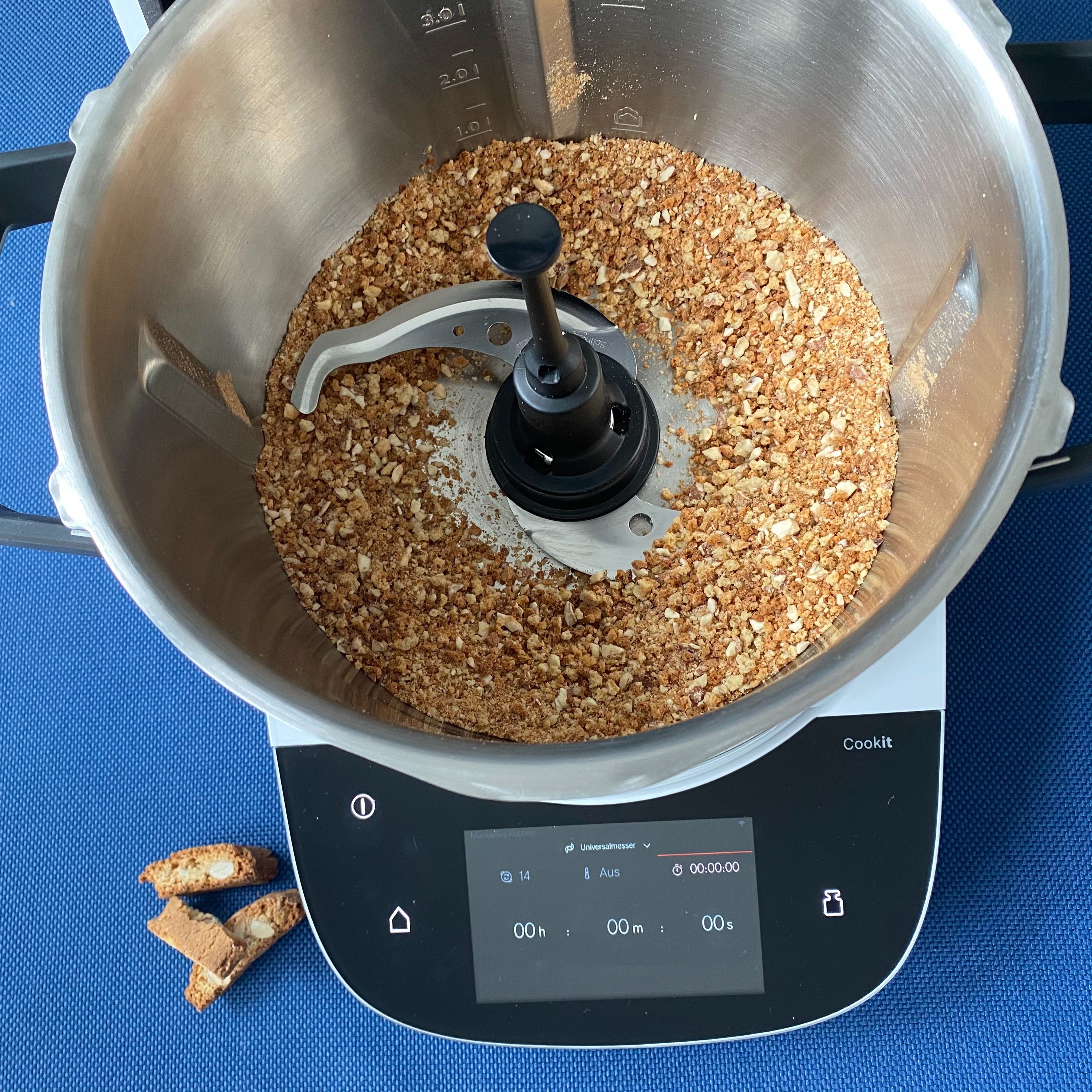 Das Cookit Universalmesser einsetzen und die Cantuccini in den Topf geben und bei geschlossenem Deckel und eingesetztem Messbecher zerkleinern (Universalmesser | Stufe 14 | 20 Sekunden). Das Universalmesser entnehmen und die Kekskrümel umfüllen.