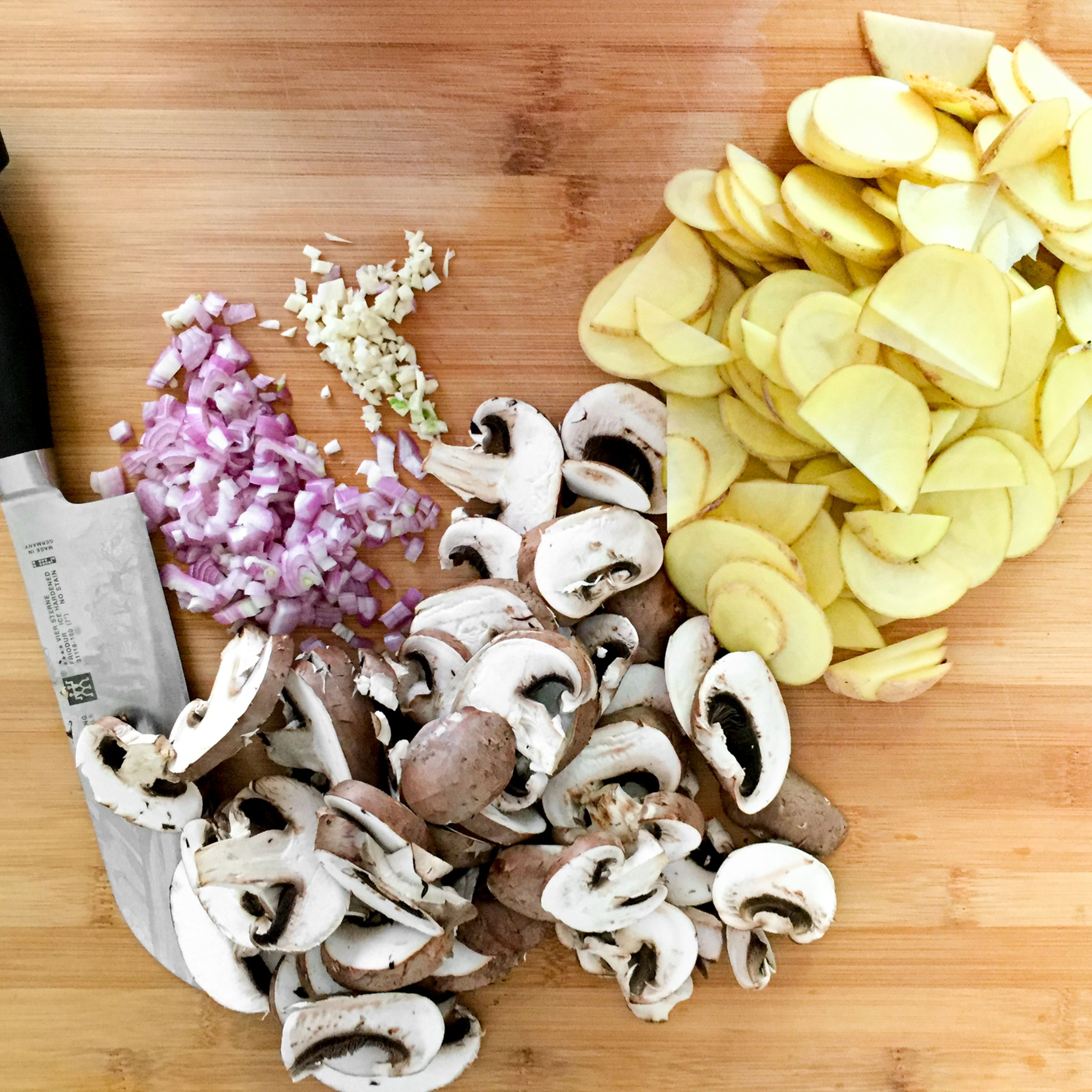 Den Ofen auf 200°C vorheizen. Die Kartoffeln schälen und in Scheiben schneiden. Zwiebel und Knoblauch fein hacken. Anschließend die Pilze in dicke Scheiben schneiden.